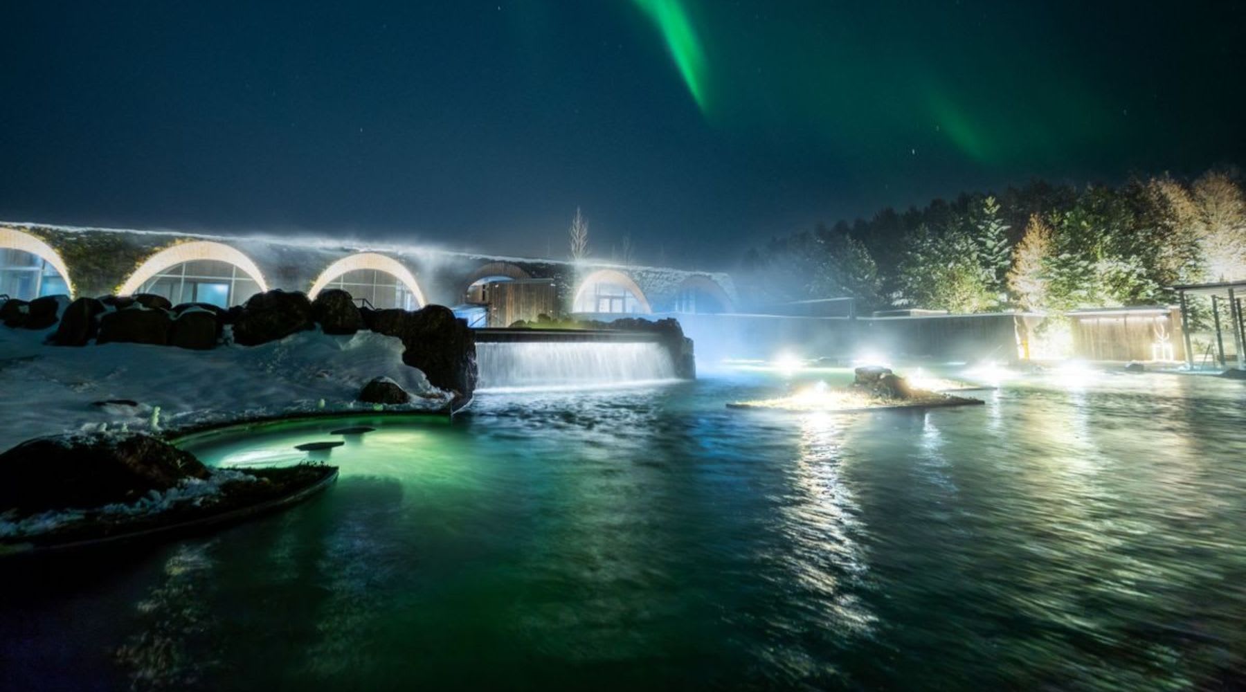 Vista nocturna del spa Laugarás con la aurora boreal en el cielo.