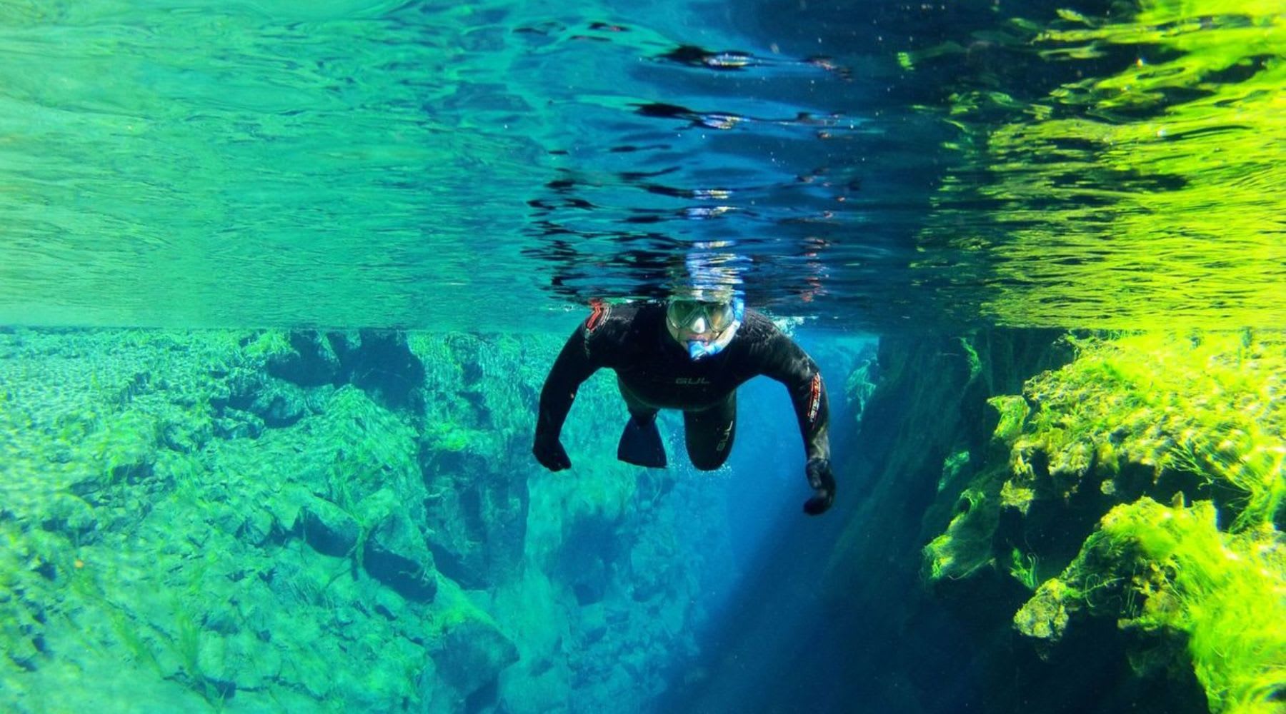 Snorkeler floating in the clear blue water of the Silfra fissure in Iceland