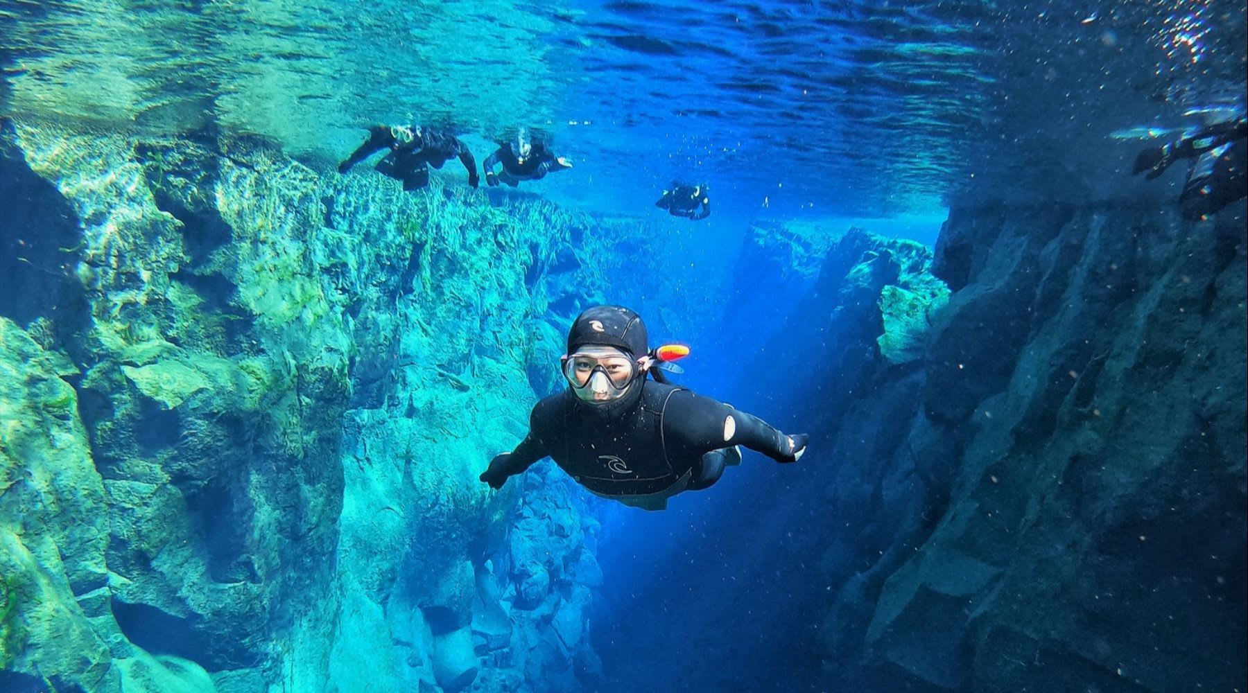 Snorkeler swimming between rocky walls in the clear waters of Silfra