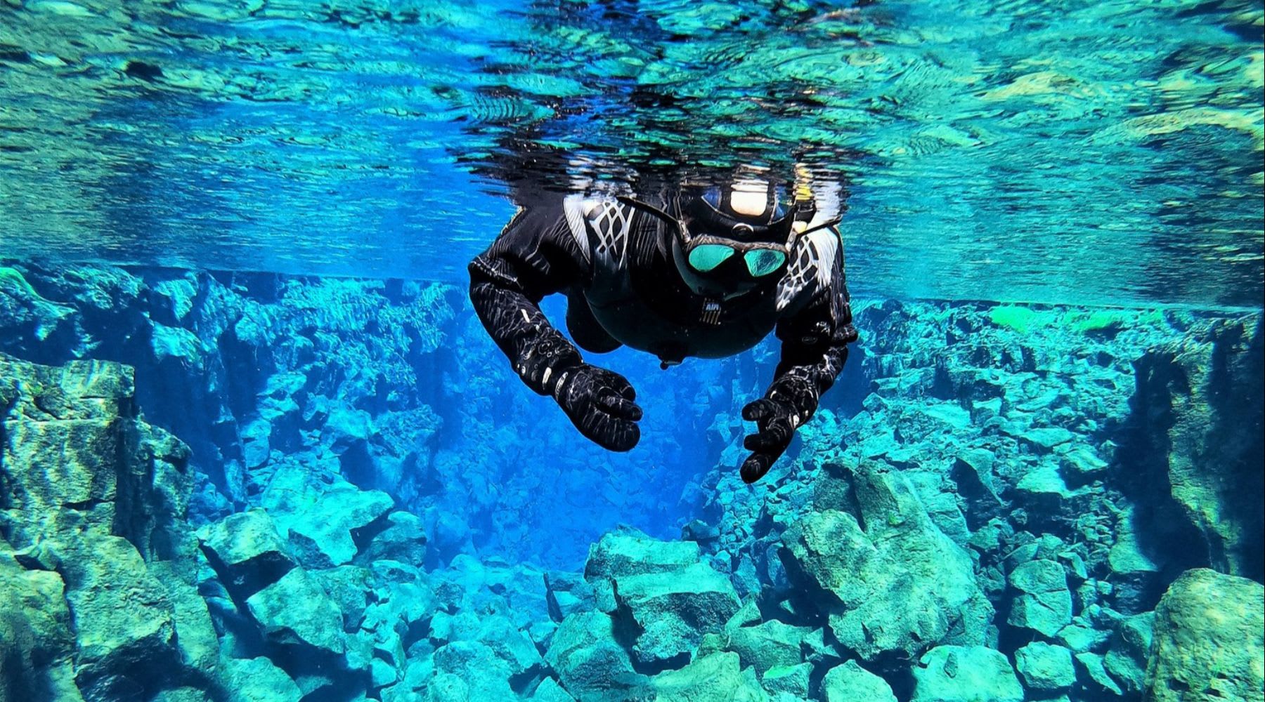 Snorkeler floating above the rocky floor of the Silfra fissure in Iceland
