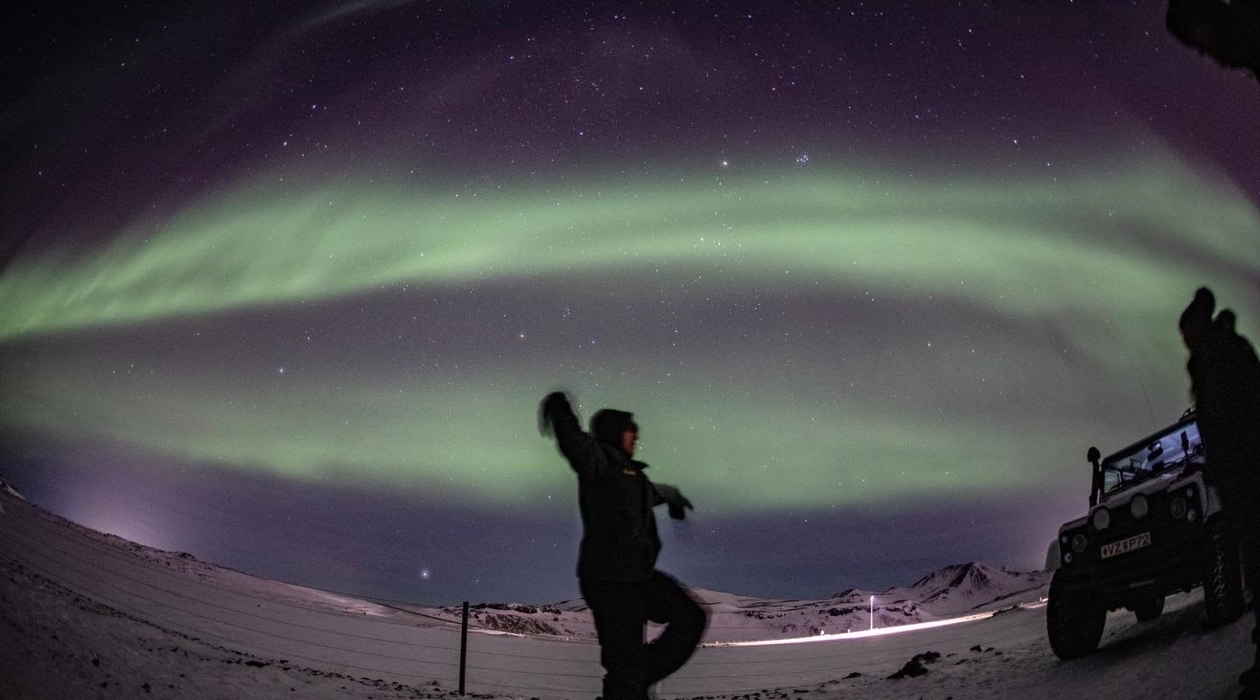 Voyageur posant sous les aurores boréales près d’un Super Jeep en Islande