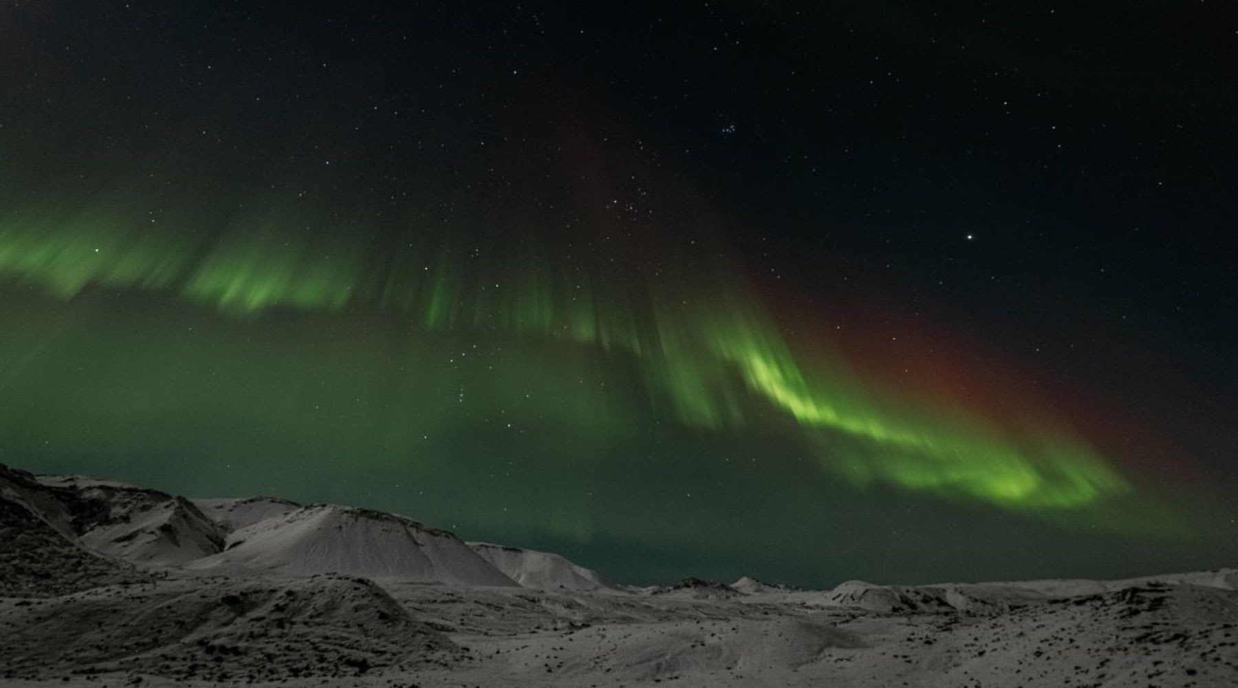 Aurores boréales illuminant un paysage montagneux enneigé en Islande