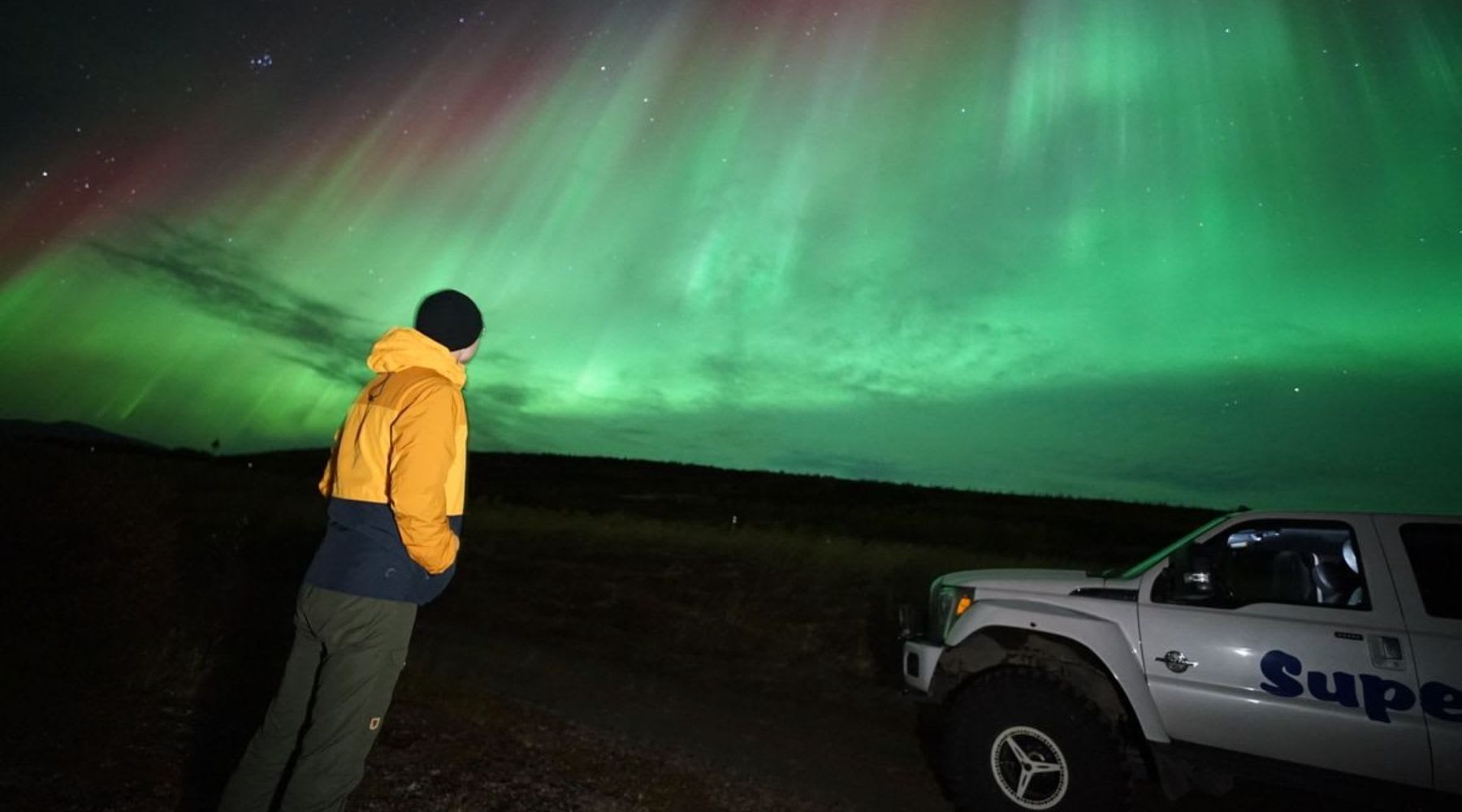 Voyageur observant les aurores boréales près d’un Super Jeep en Islande