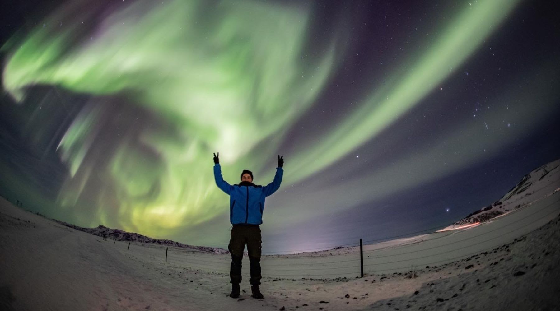 Voyageur debout dans la neige sous de vives aurores boréales