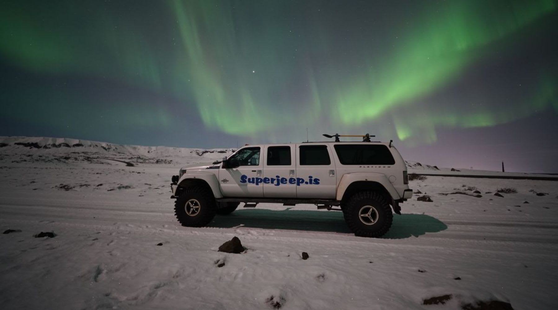 Super Jeep garé sur la neige sous des aurores boréales vertes en Islande