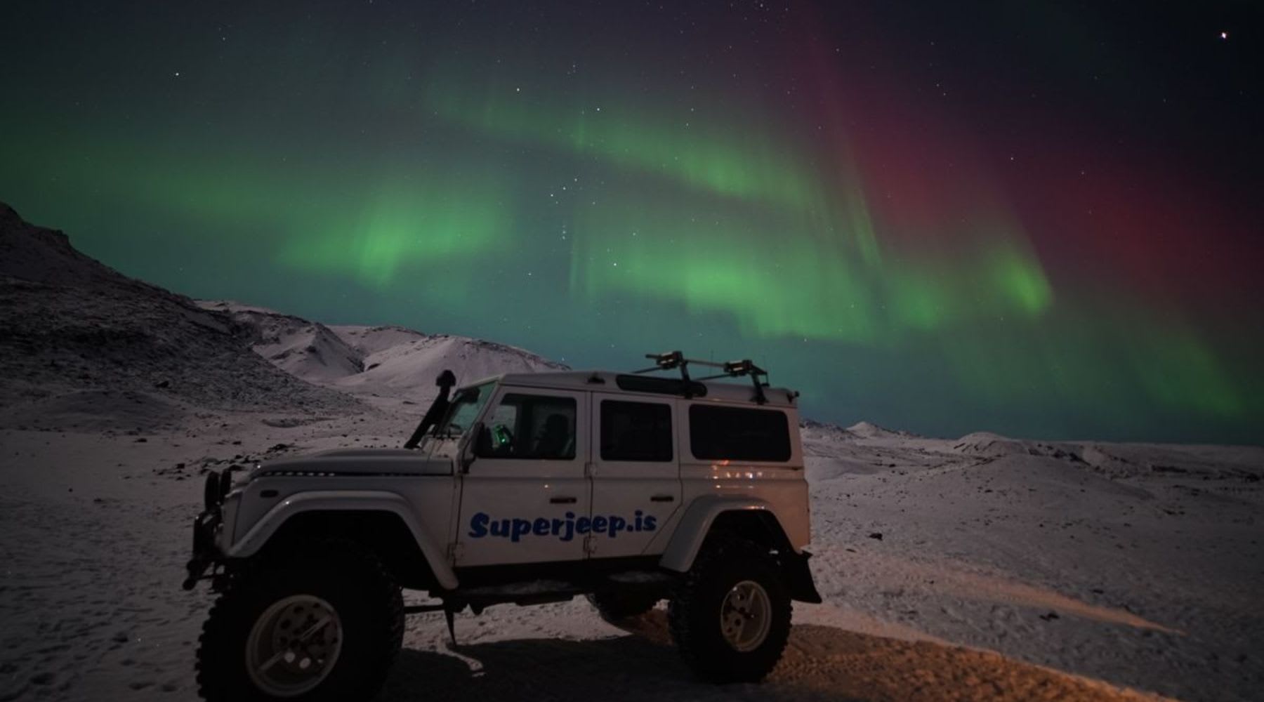 Super Jeep in einer verschneiten isländischen Landschaft unter den Nordlichtern