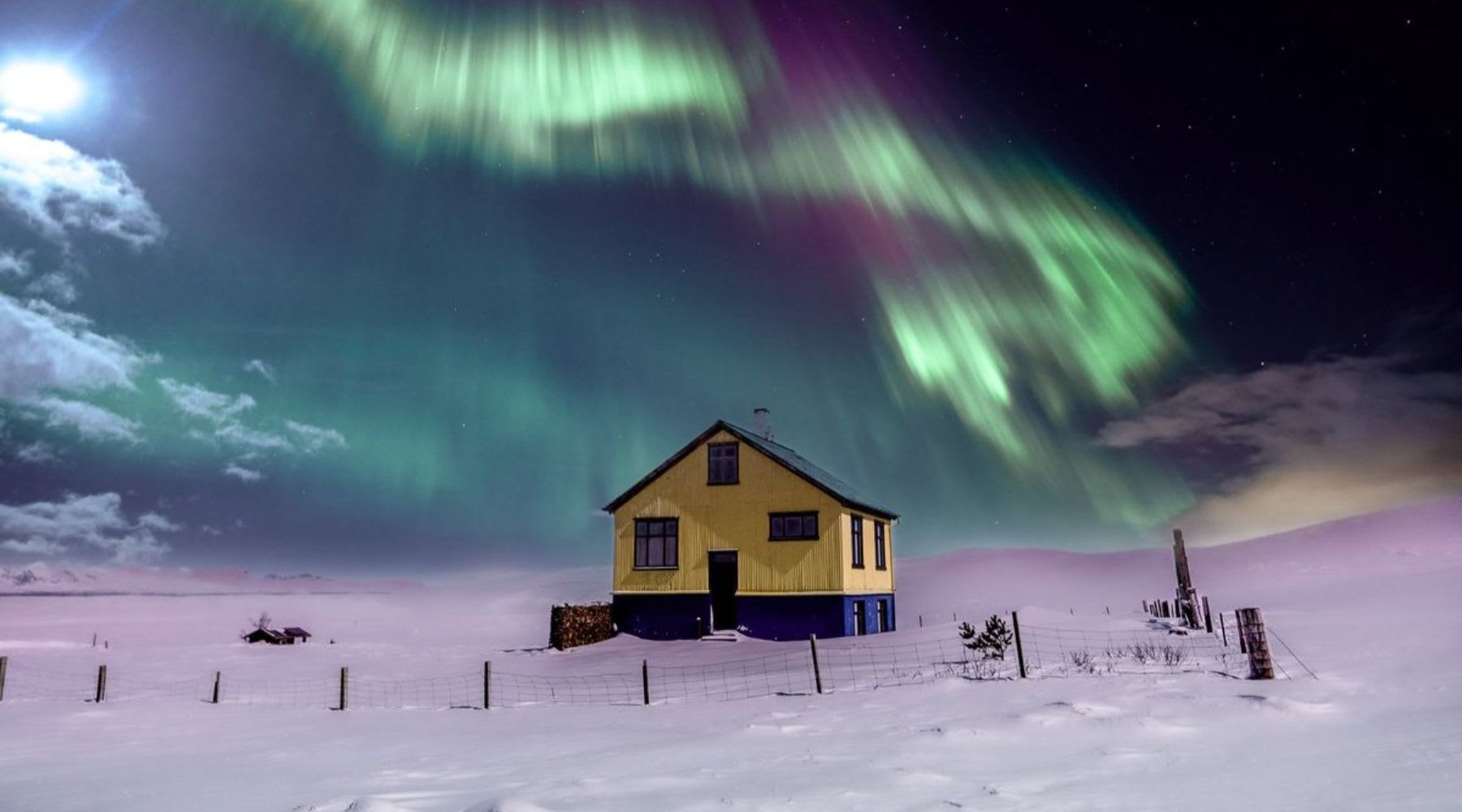 Northern lights shining over a yellow house in a snowy Icelandic landscape