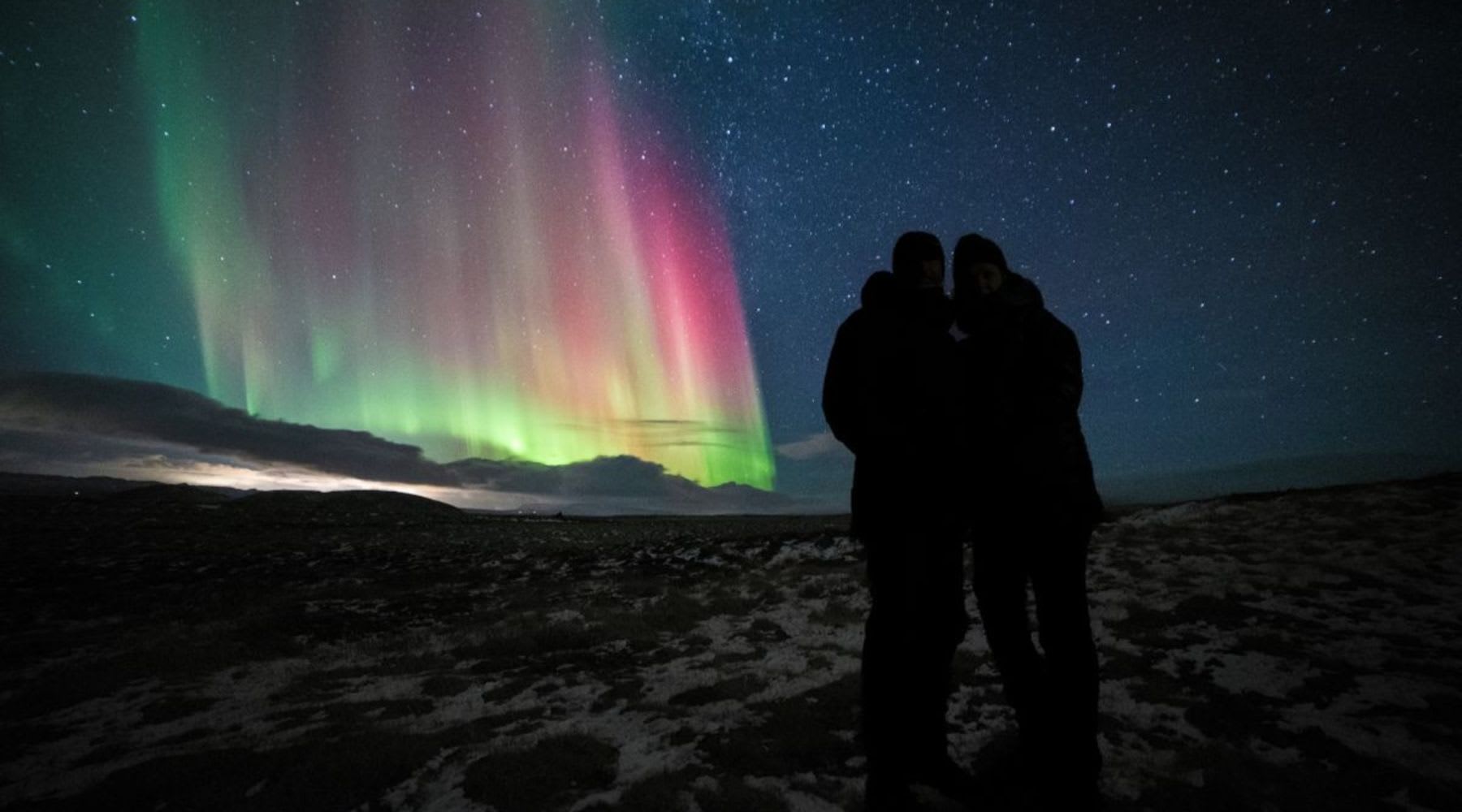 Couple standing under colorful northern lights in a snowy Icelandic landscape