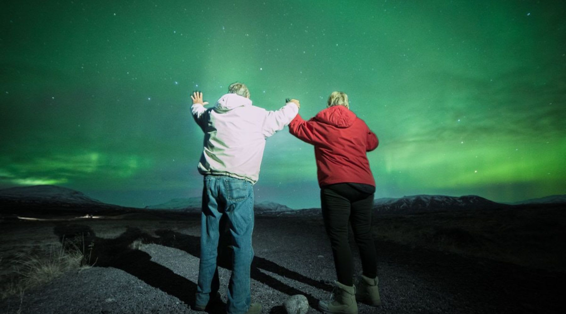 Two travelers holding hands under green northern lights in Iceland