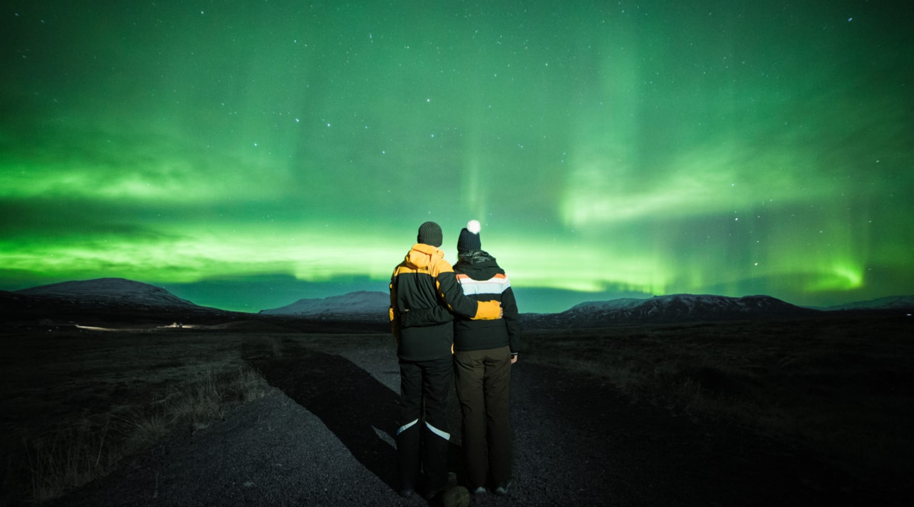Couple standing together under bright green northern lights in Iceland