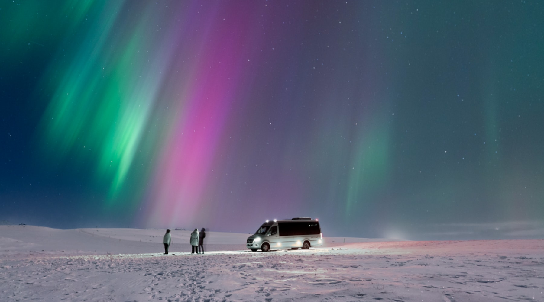 Small group watching colorful northern lights beside a minivan in the snow
