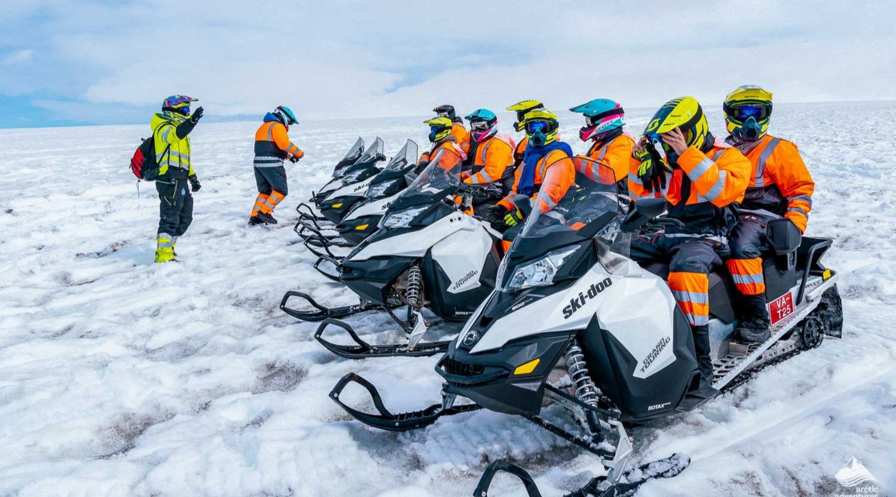 Gruppo di motoslitte con clienti in tute arancioni, pronti a partire per l'avventura.