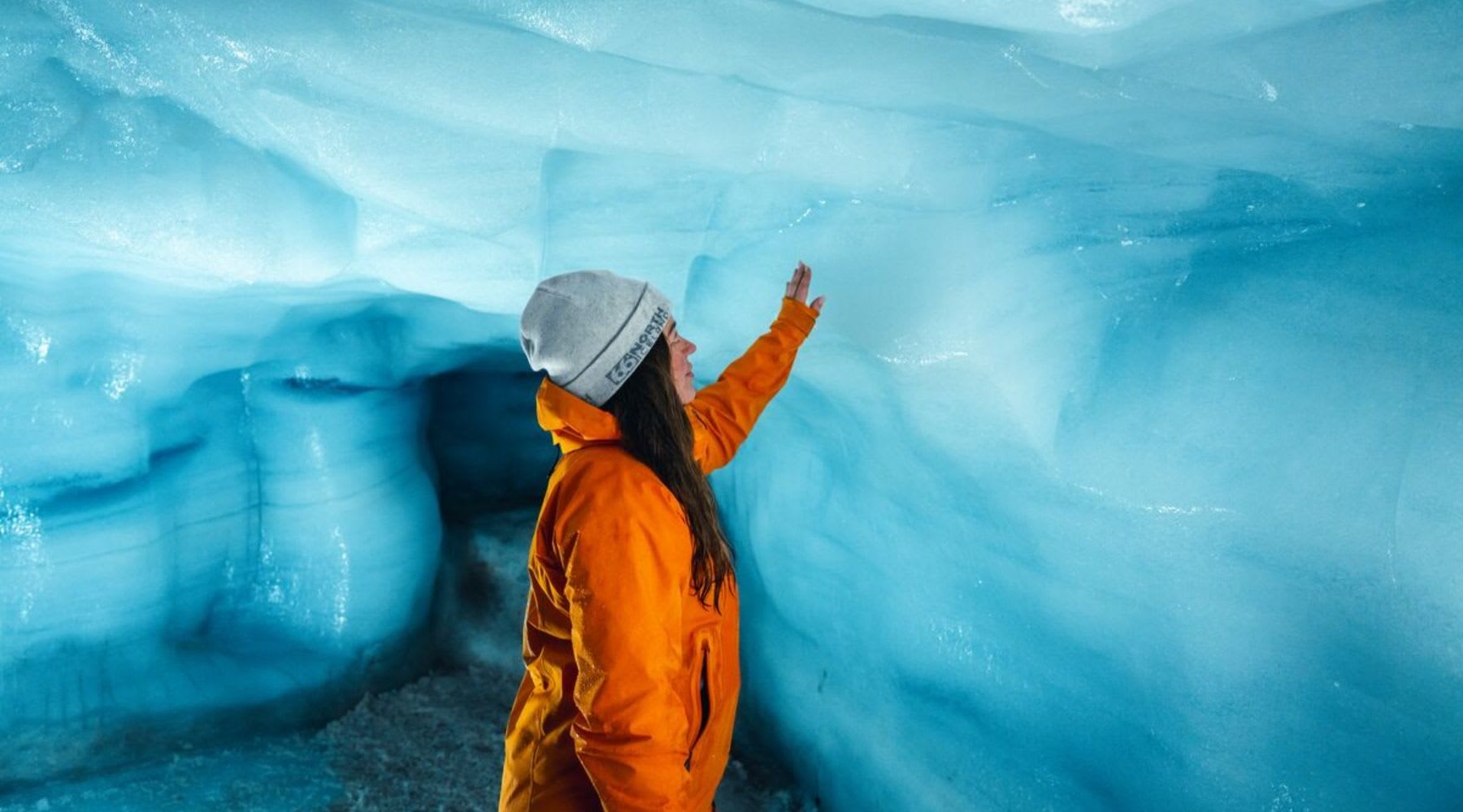 Turista che tocca le pareti di ghiaccio all'interno di una cavità glaciale.