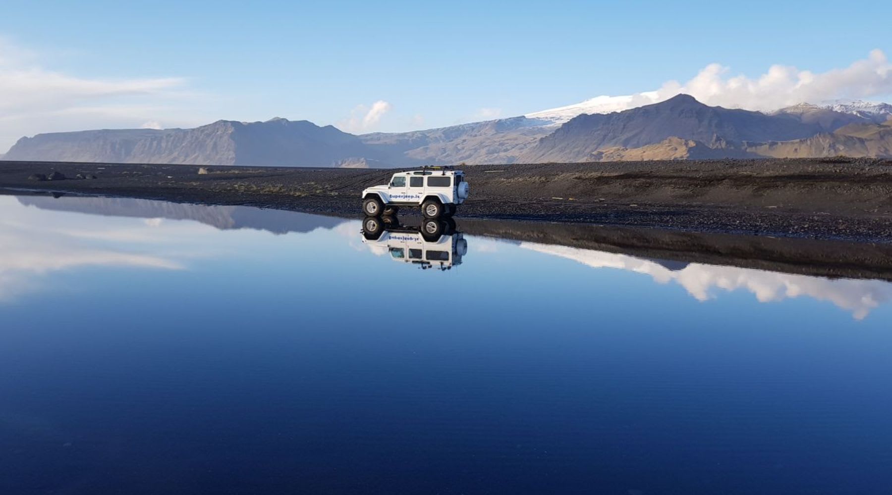 White super jeep parked in front of a glacial lake.