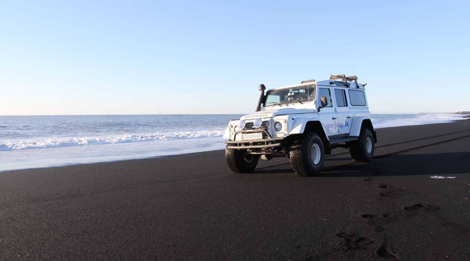Super-Jeep mit Schnorchel an einem schwarzen Sandstrand.