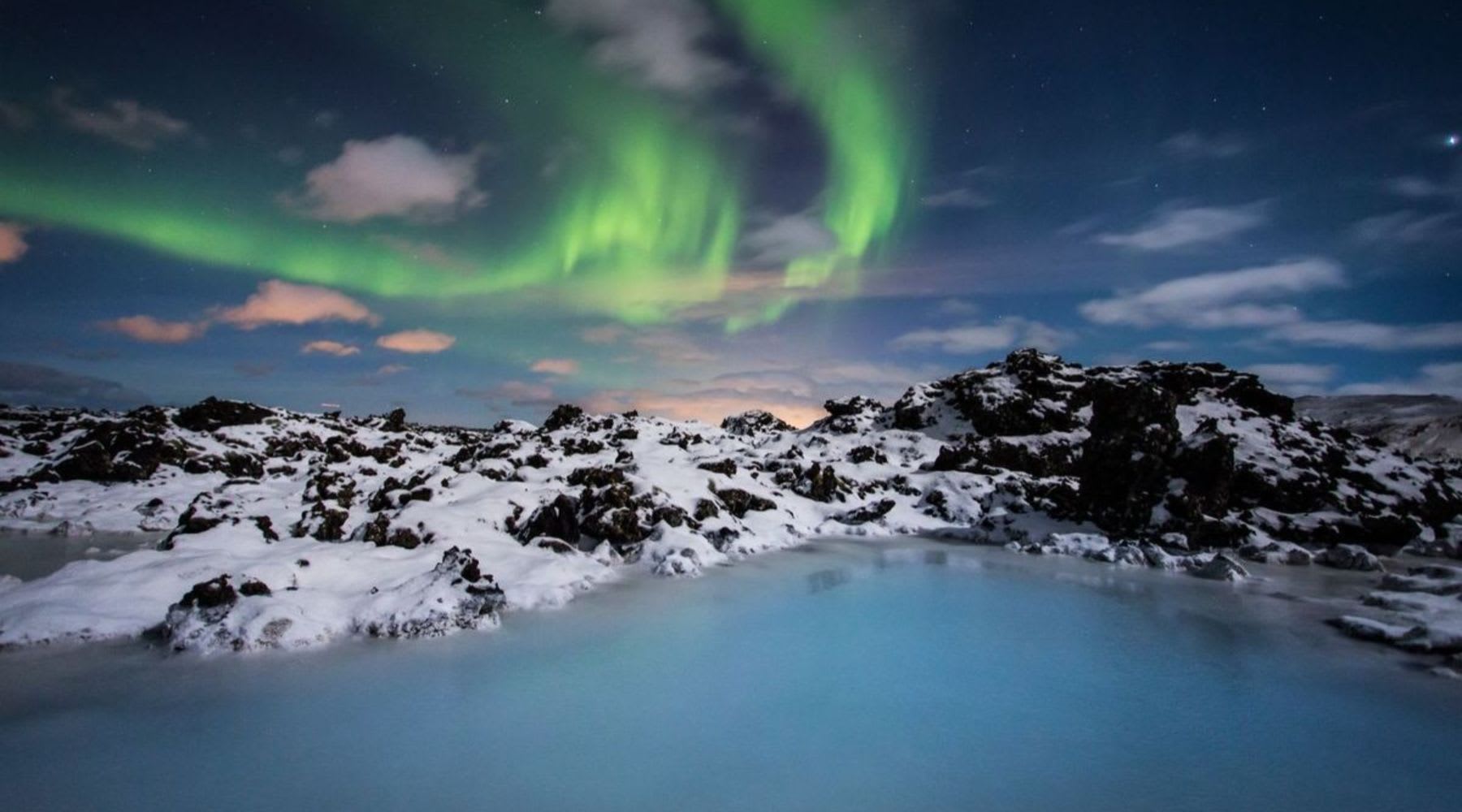 Northern lights glowing above the Blue Lagoon in a snowy Icelandic landscape