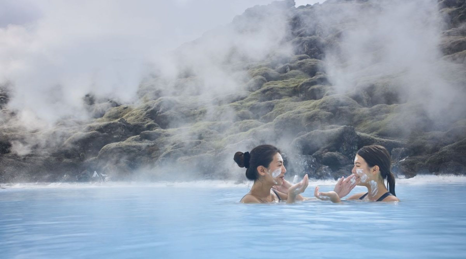 Two women applying silica masks while bathing in the Blue Lagoon