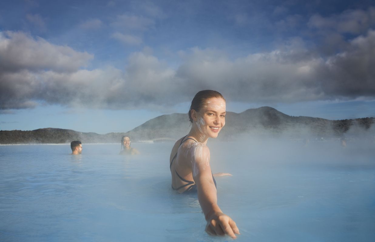Mujer sonriendo en las aguas azules y vaporosas de la Blue Lagoon con una mascarilla de sílice en la cara
