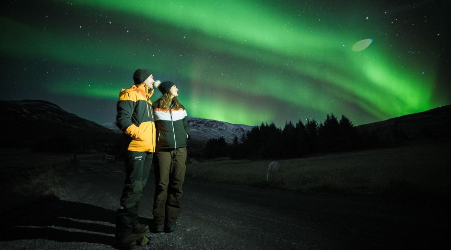Couple observant les aurores boréales au-dessus d’une route de montagne en Islande