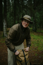 Mann in Outdoor-Kleidung steht in einem Wald und lächelt in die Kamera