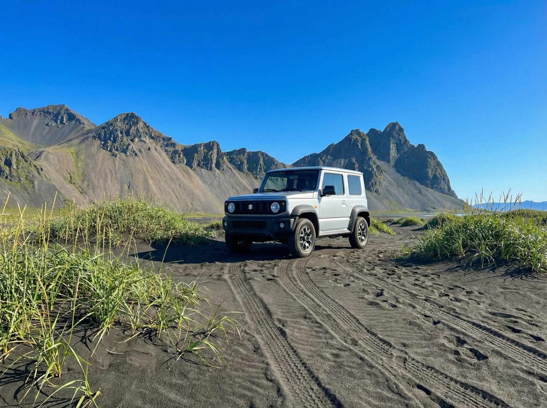 4x4-køretøj parkeret på sort vulkansk sand med bjerge i det fjerne under en klar blå himmel