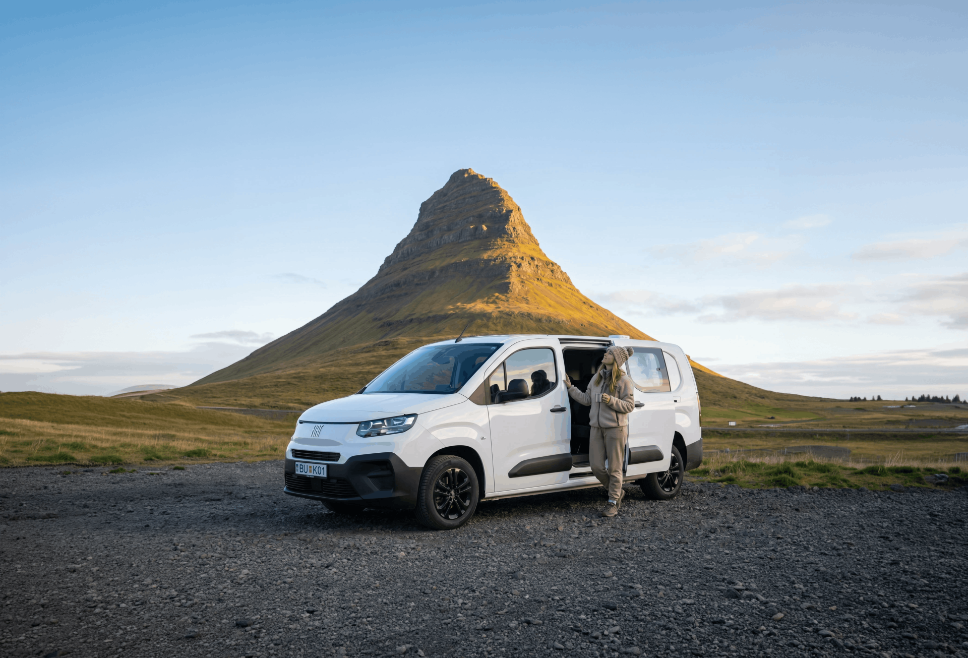 Person som står bredvid en vit husbil parkerad framför berget Kirkjufell
