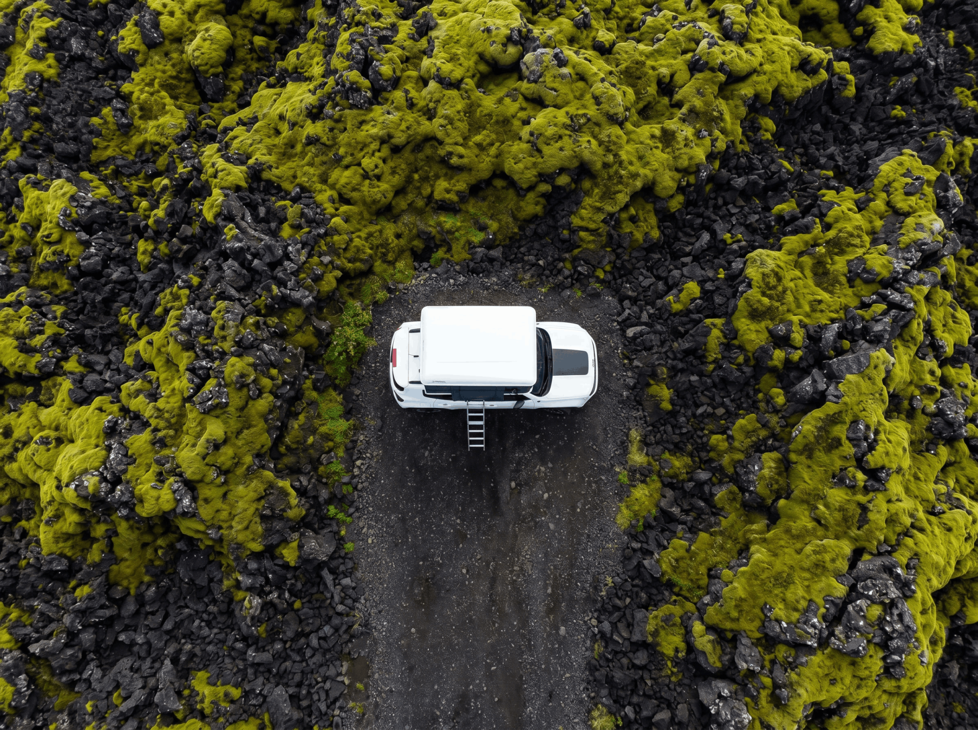 Luftfoto af en hvid 4x4 med et tagtelt parkeret på mosbegroet lavaterræn