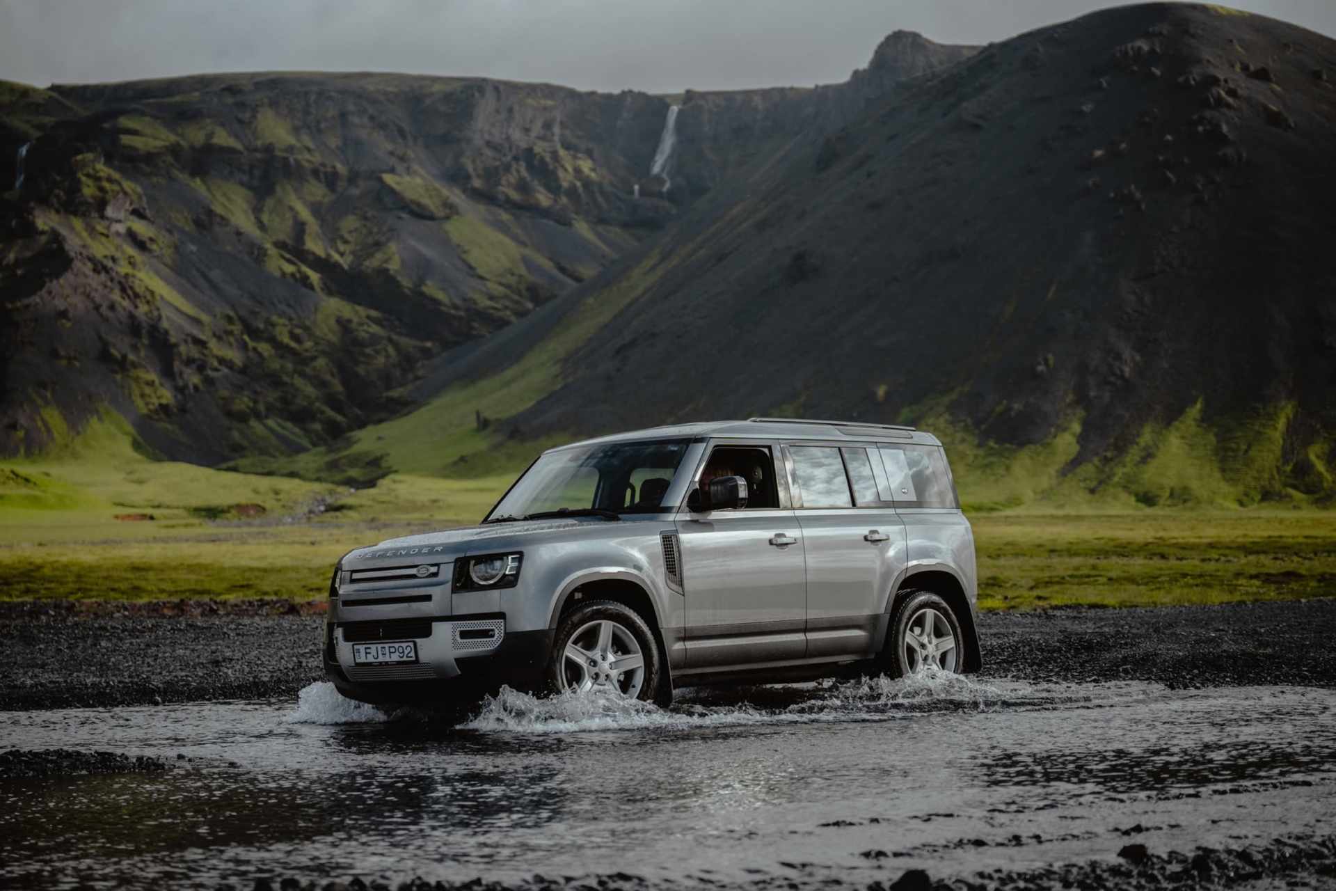 SUV blanco circulando por una carretera islandesa con montañas nevadas al fondo