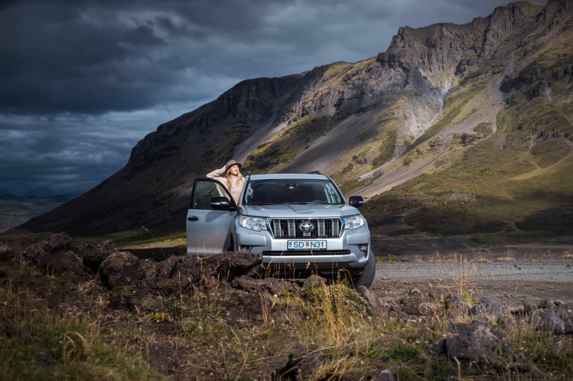 SUV blanco circulando por una carretera islandesa con montañas nevadas al fondo