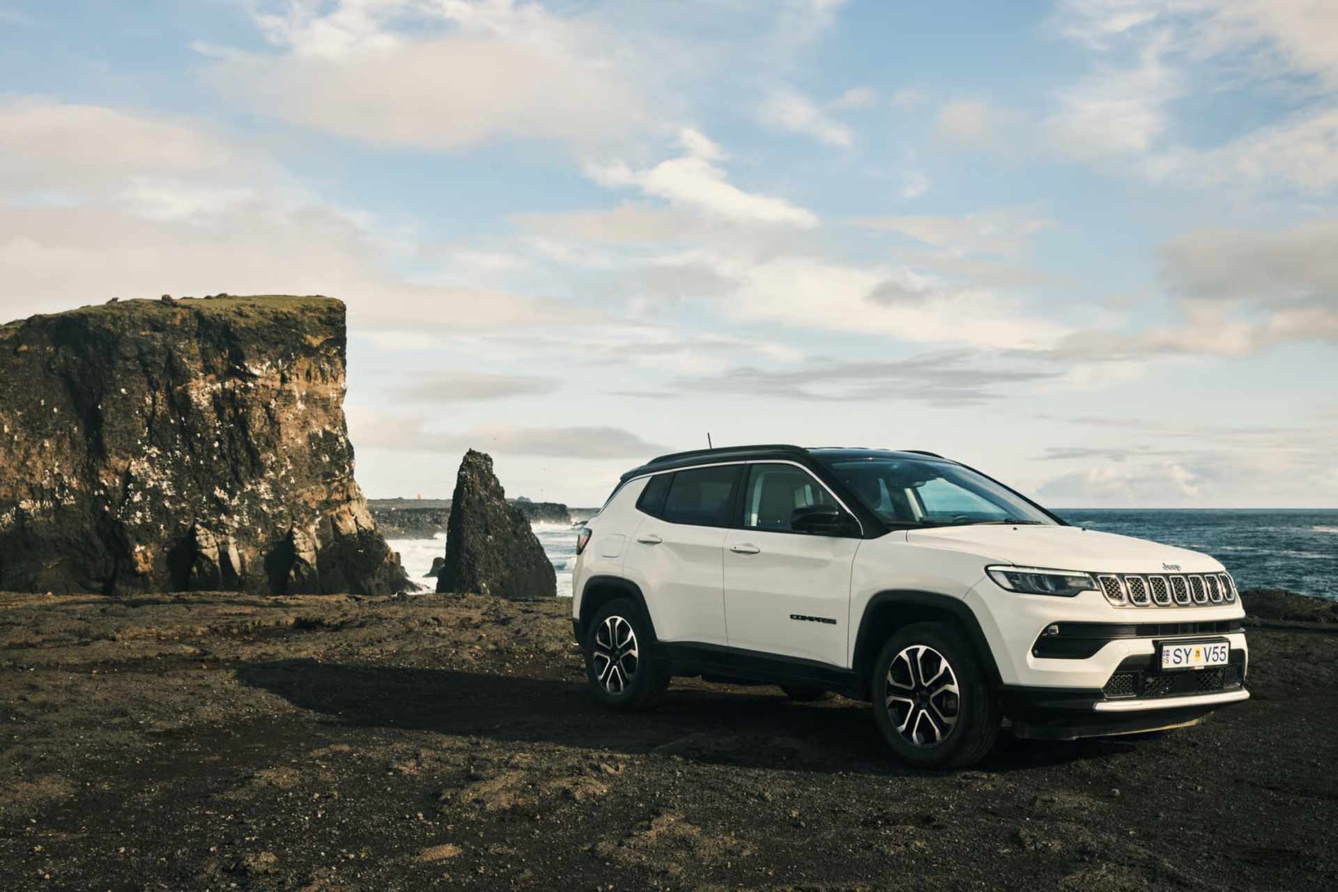 Hvid SUV kører på en islandsk vej med snedækkede bjerge i baggrunden
