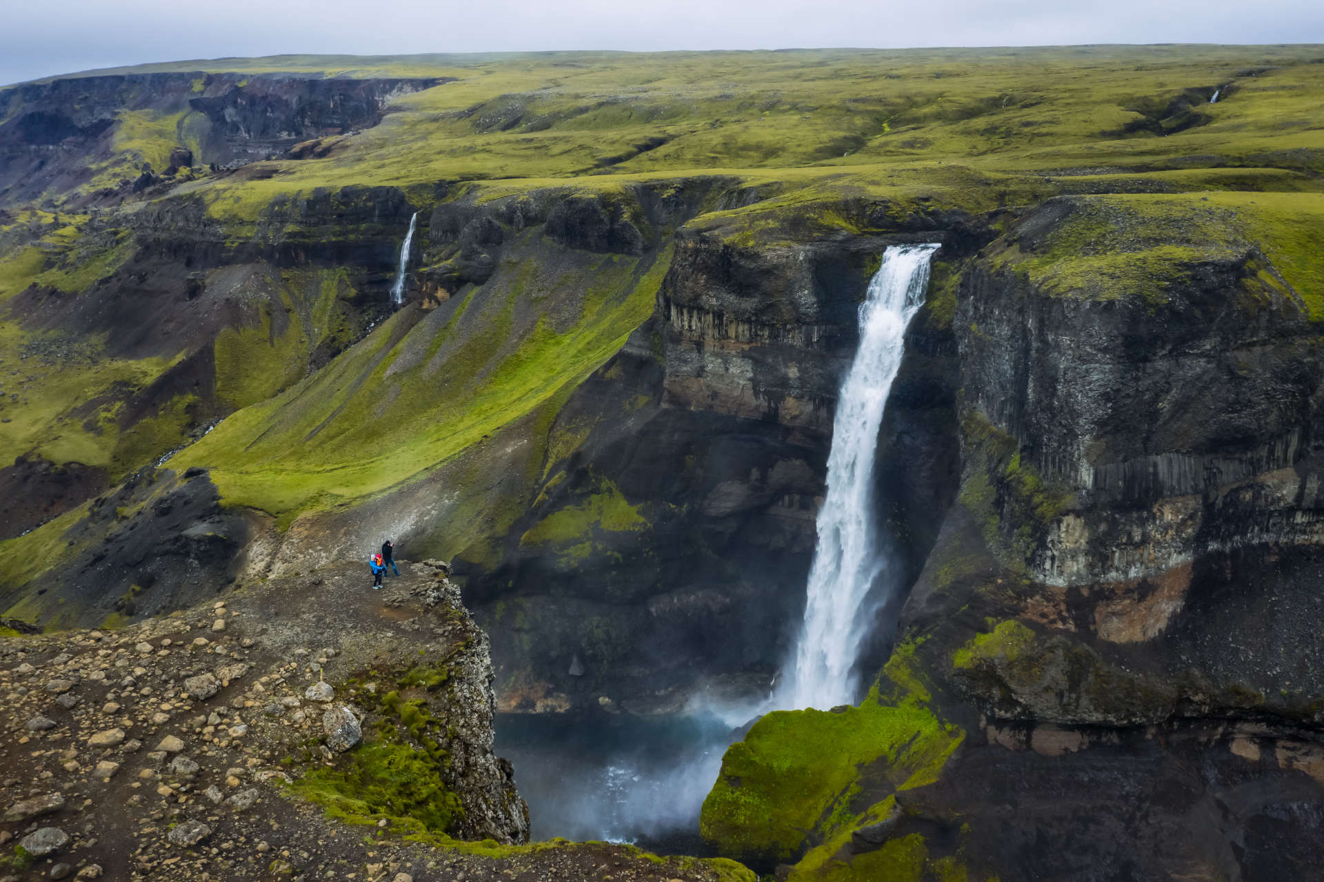 Wide waterfall cascading over a green cliff edge in the Icelandic countryside