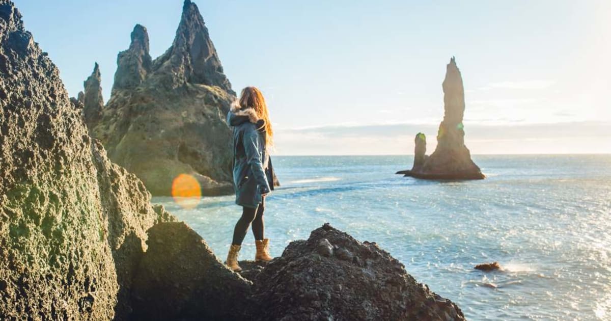 Woman overlooking Reynisdrangar sea stacks and Iceland’s rugged coast, inspiring UK travellers to explore dramatic beaches and ocean views