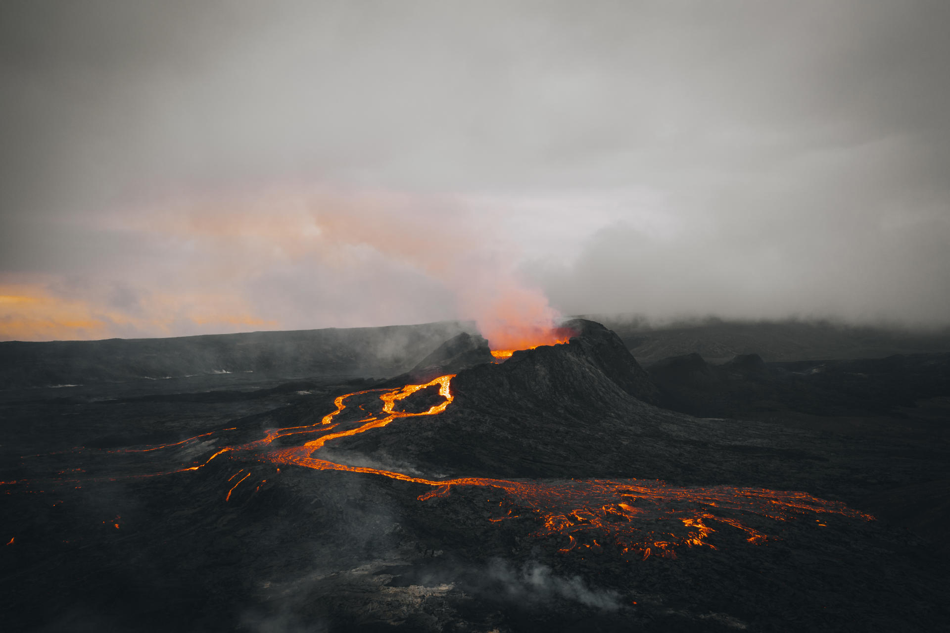 Luftaufnahme eines ausbrechenden Vulkans in der Abenddämmerung mit glühender Lava auf dunklem Gelände