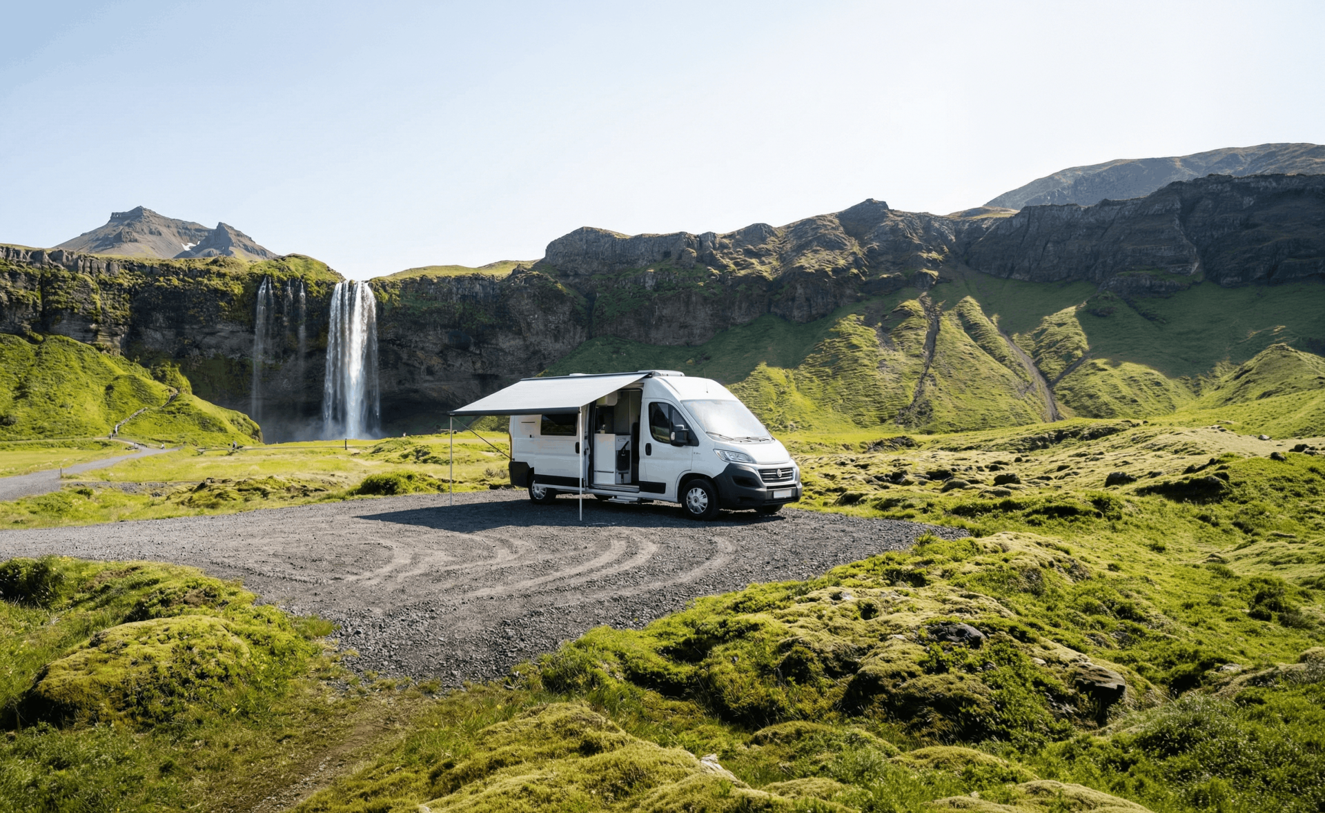 Wohnmobil parkt neben einem Wasserfall, umgeben von grünen Hügeln