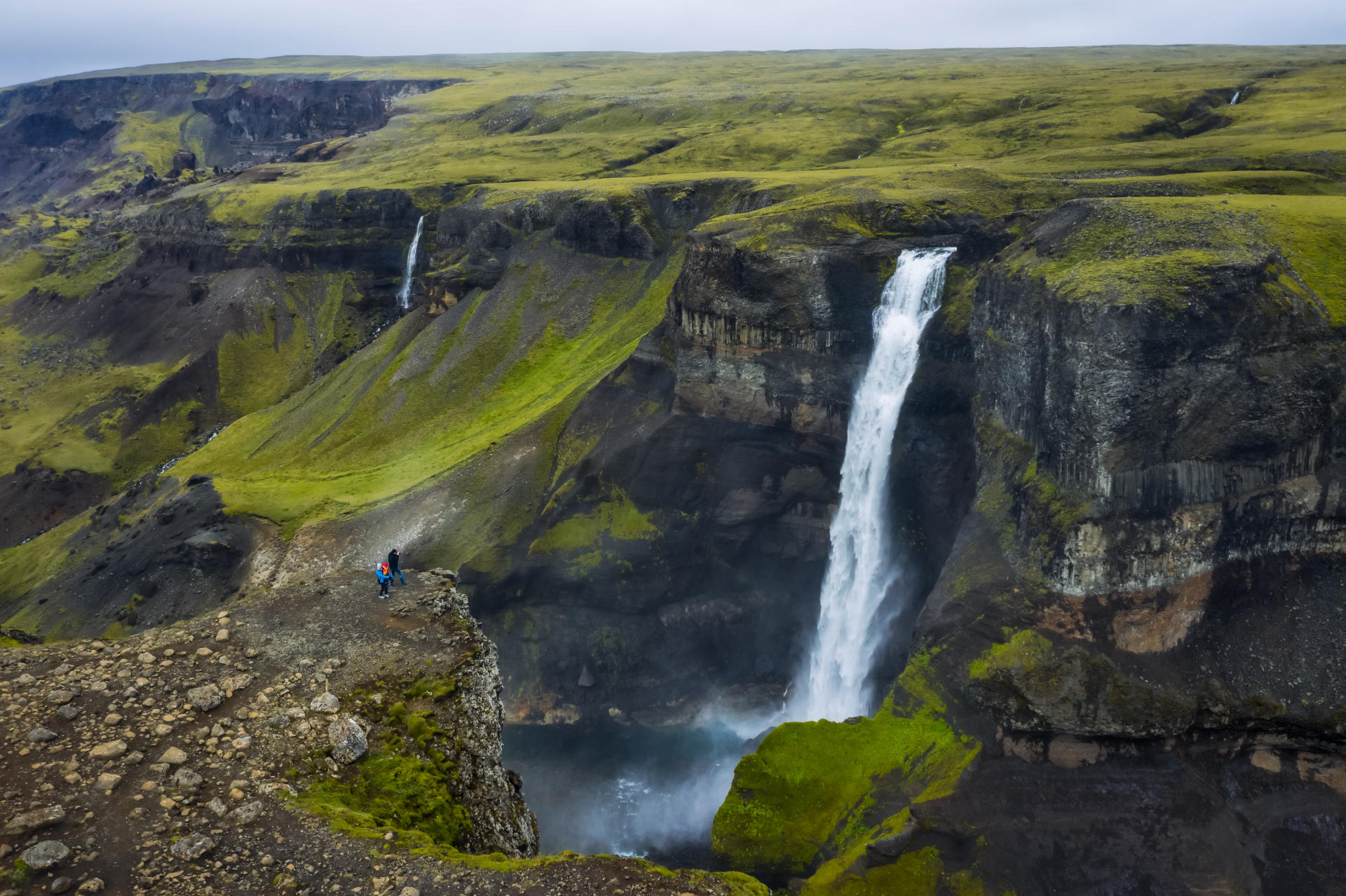 Breiter Wasserfall stürzt über eine grüne Klippe in der isländischen Landschaft