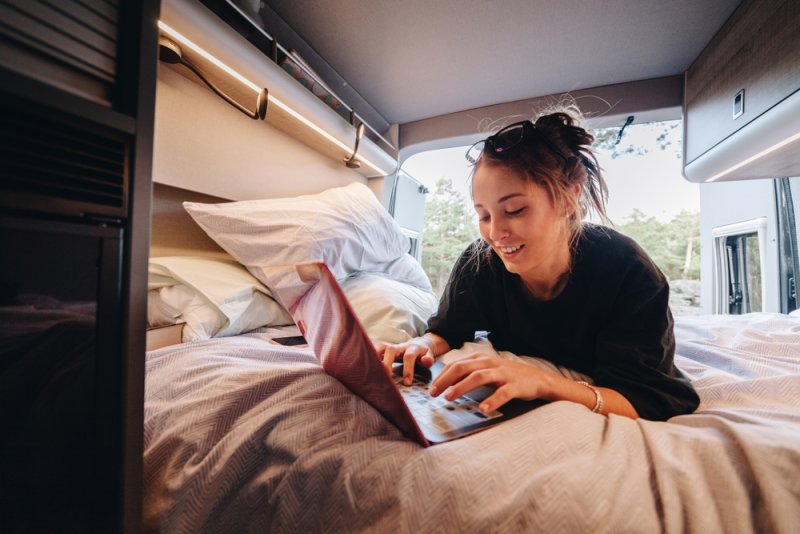 Donna sdraiata su un letto all'interno di un camper, che usa un laptop