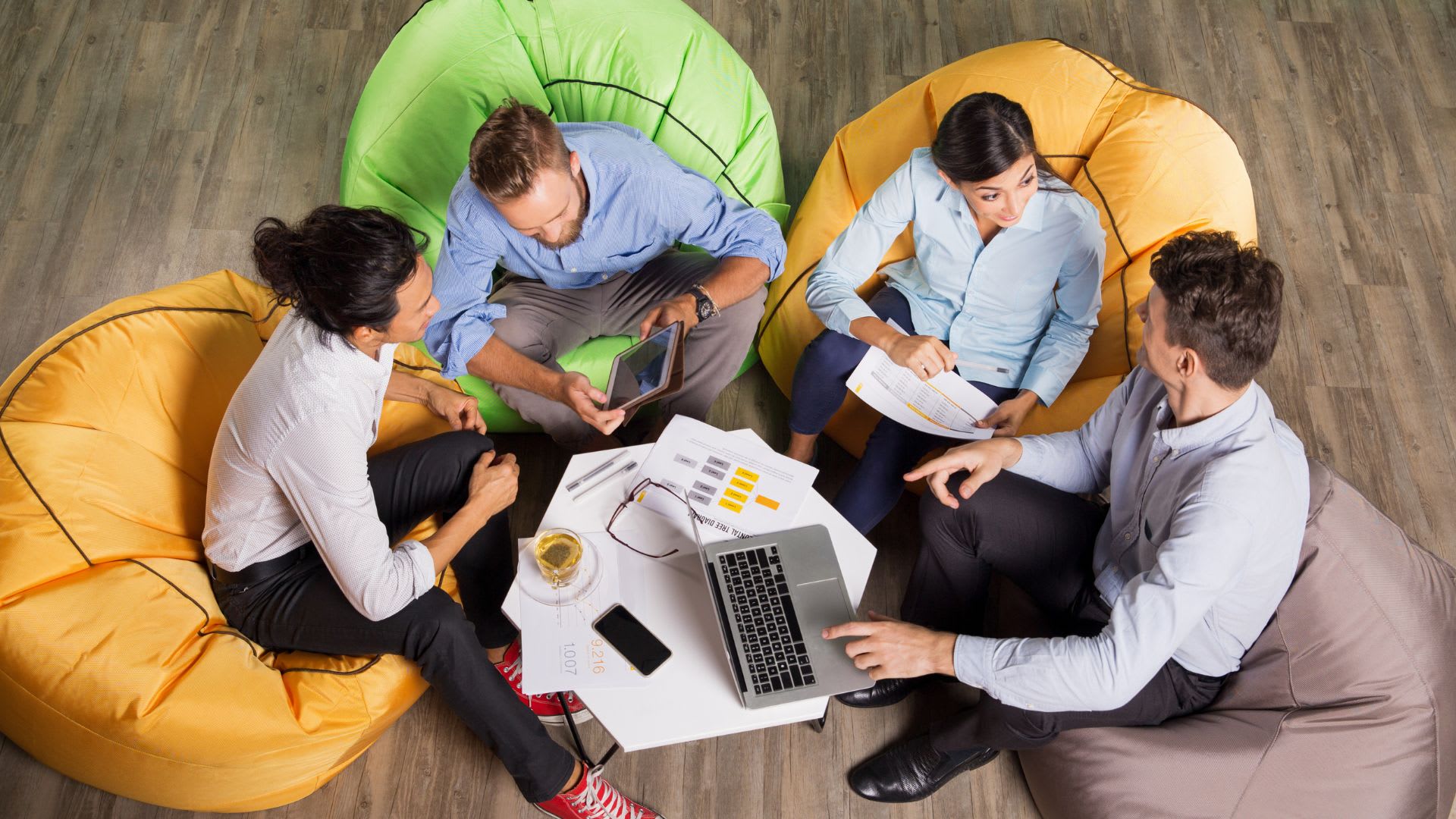 4 colleagues chatting happily in an office with pointing to their laptops and documents