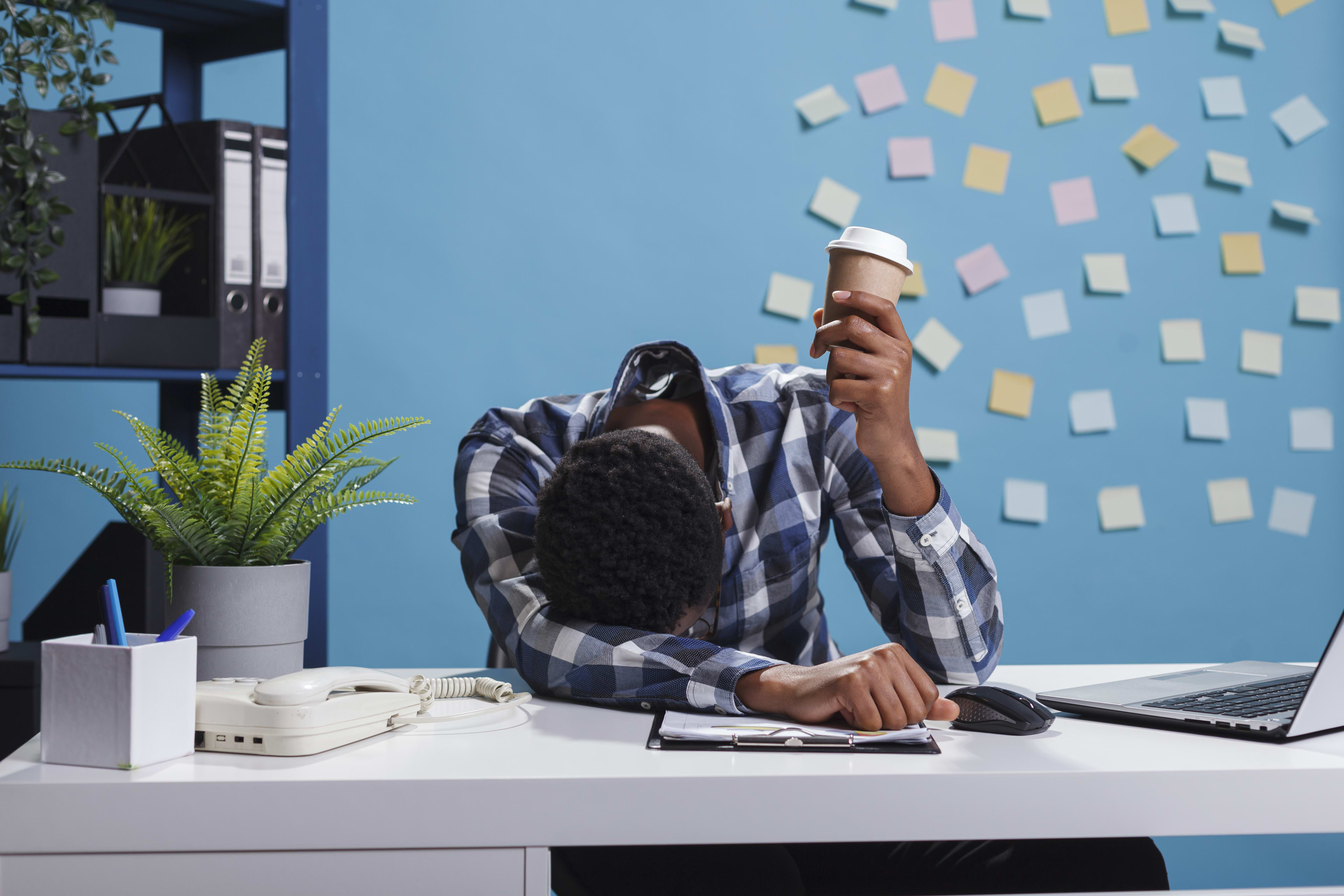 Stressed, fatigued employee sitting with head under hands at desk