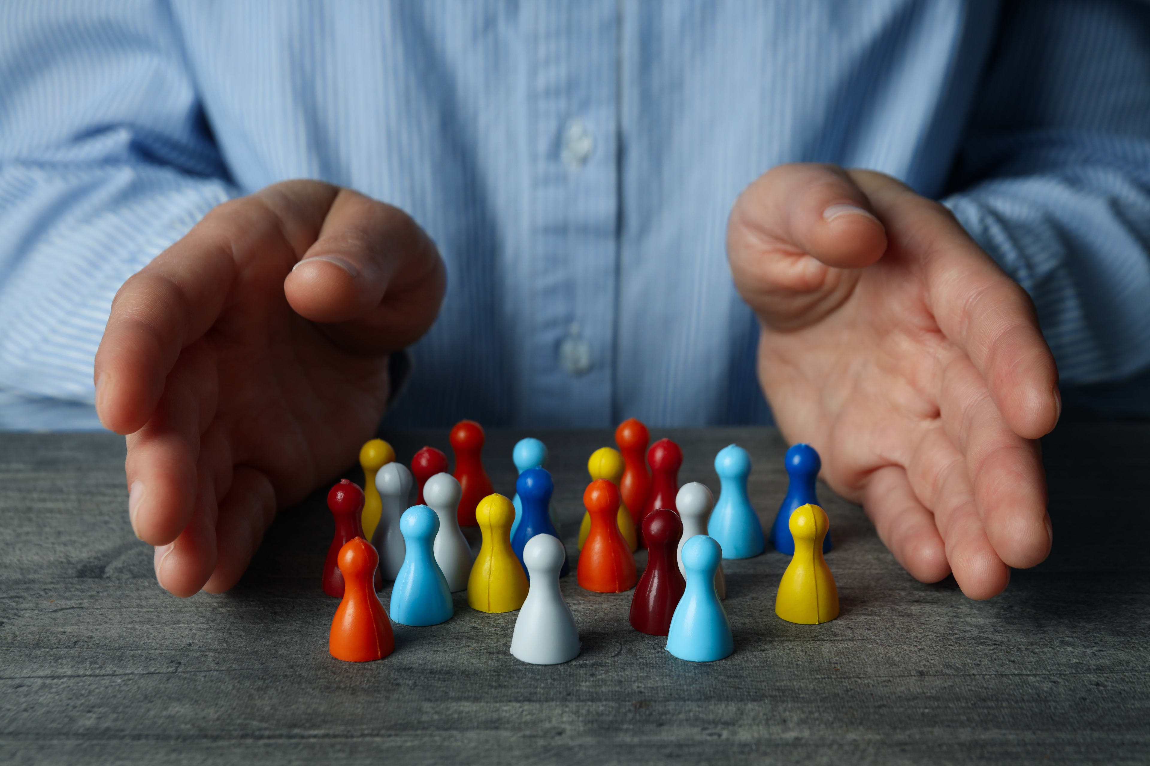 Conceptual photo of diversity with pawns of varying colors in front of a persons palms open as if gathering them towards one direction