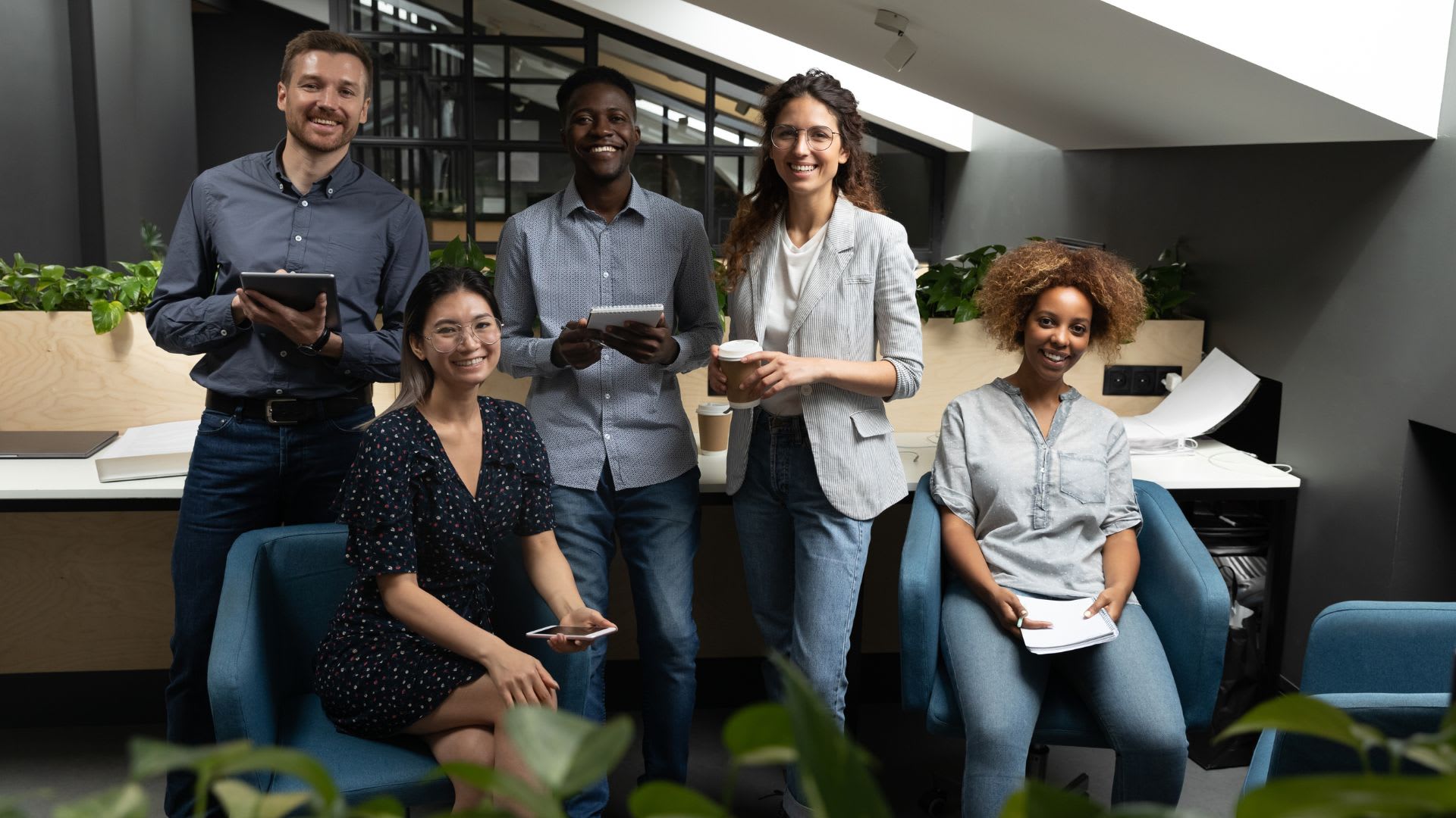 Diverse team of professionals standing or sitting next to each other in the workplace - looking at the camera smiling. 
