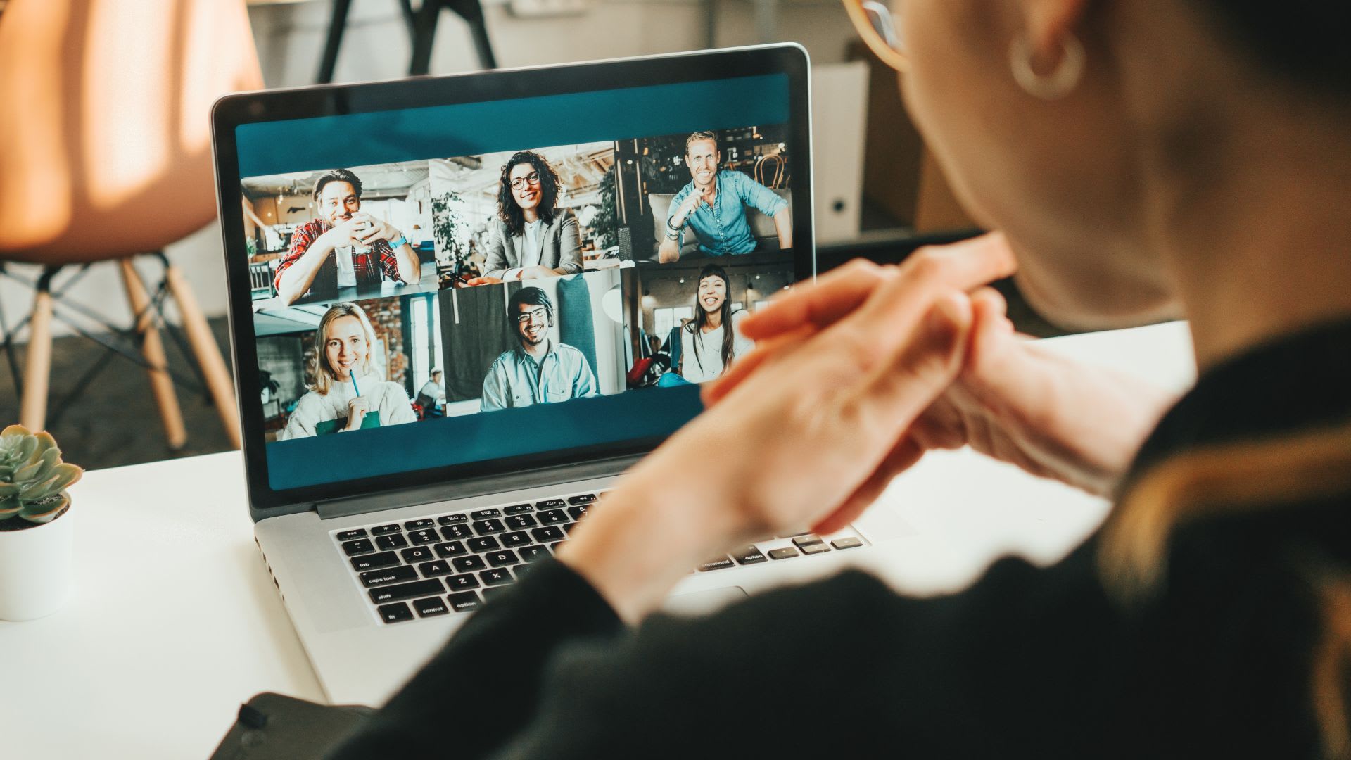 A woman focused on a laptop screen displaying a group of people.