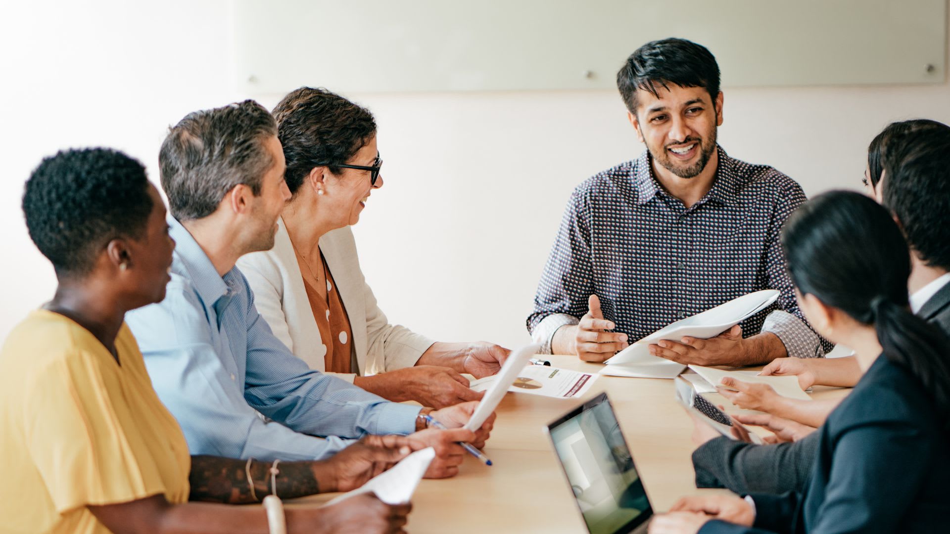 A diverse group of individuals gathered around a table, engrossed in their work, surrounded by papers and documents.