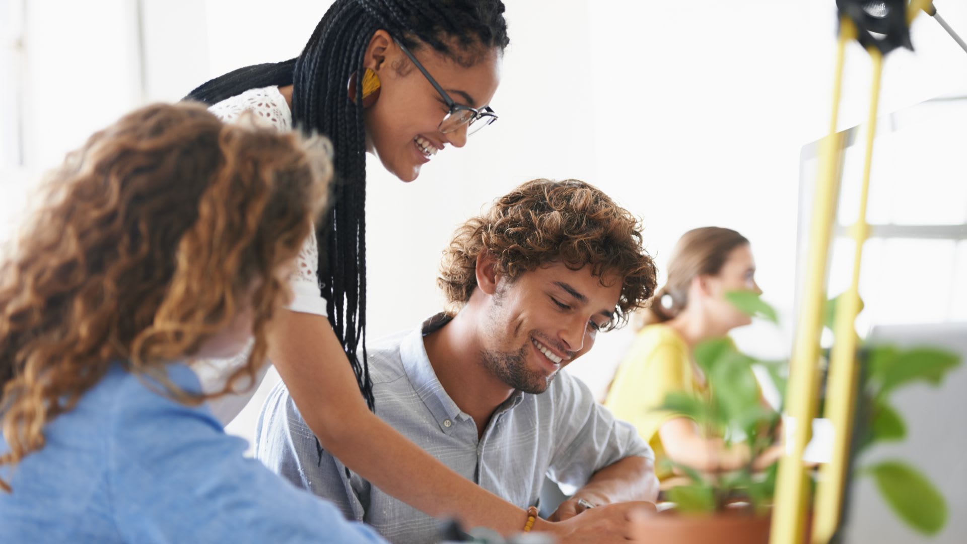 Group of three people gathered around a computer, engaged in teamwork.