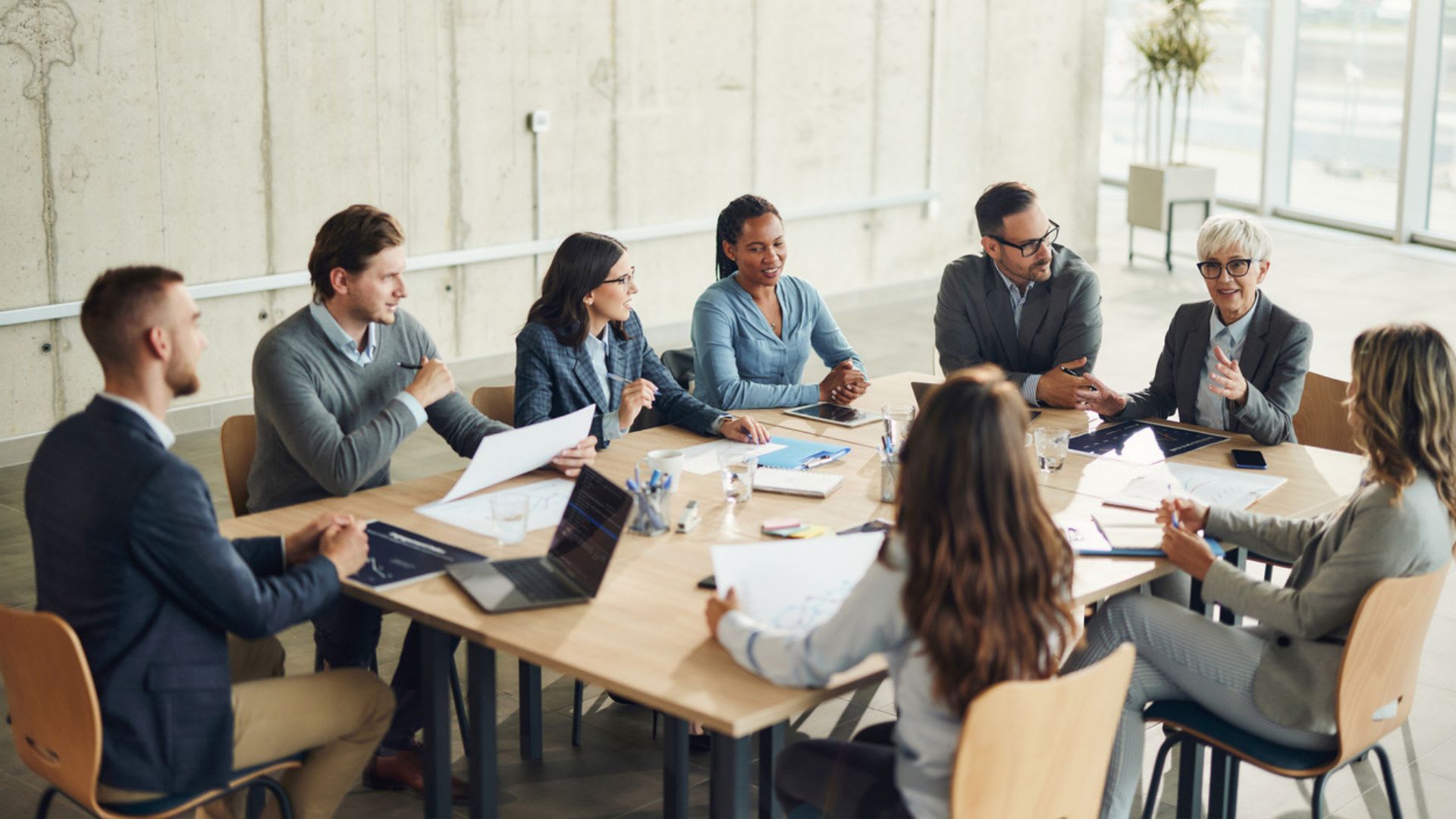 A diverse group of professionals in business attire sitting around a conference table discussing ideas.