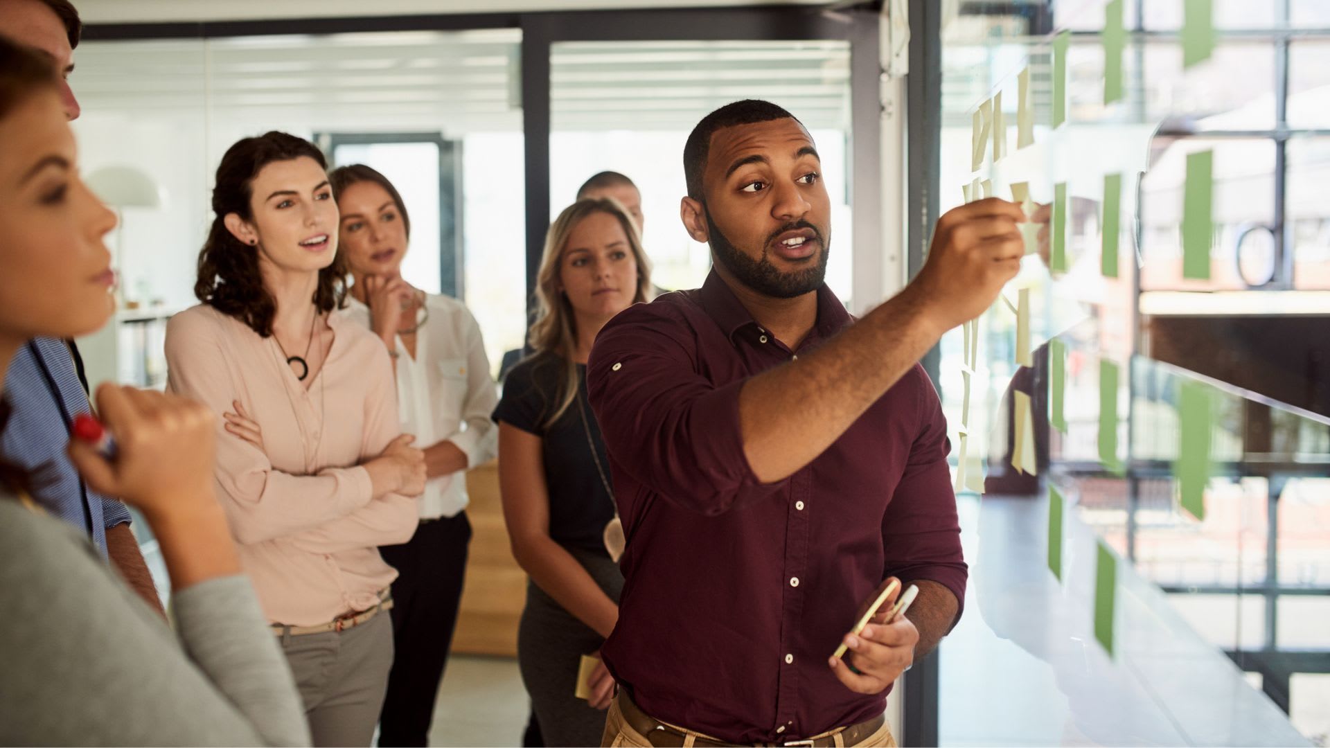 A group of people gathered around a man pointing at a board, engaged in a discussion or presentation.