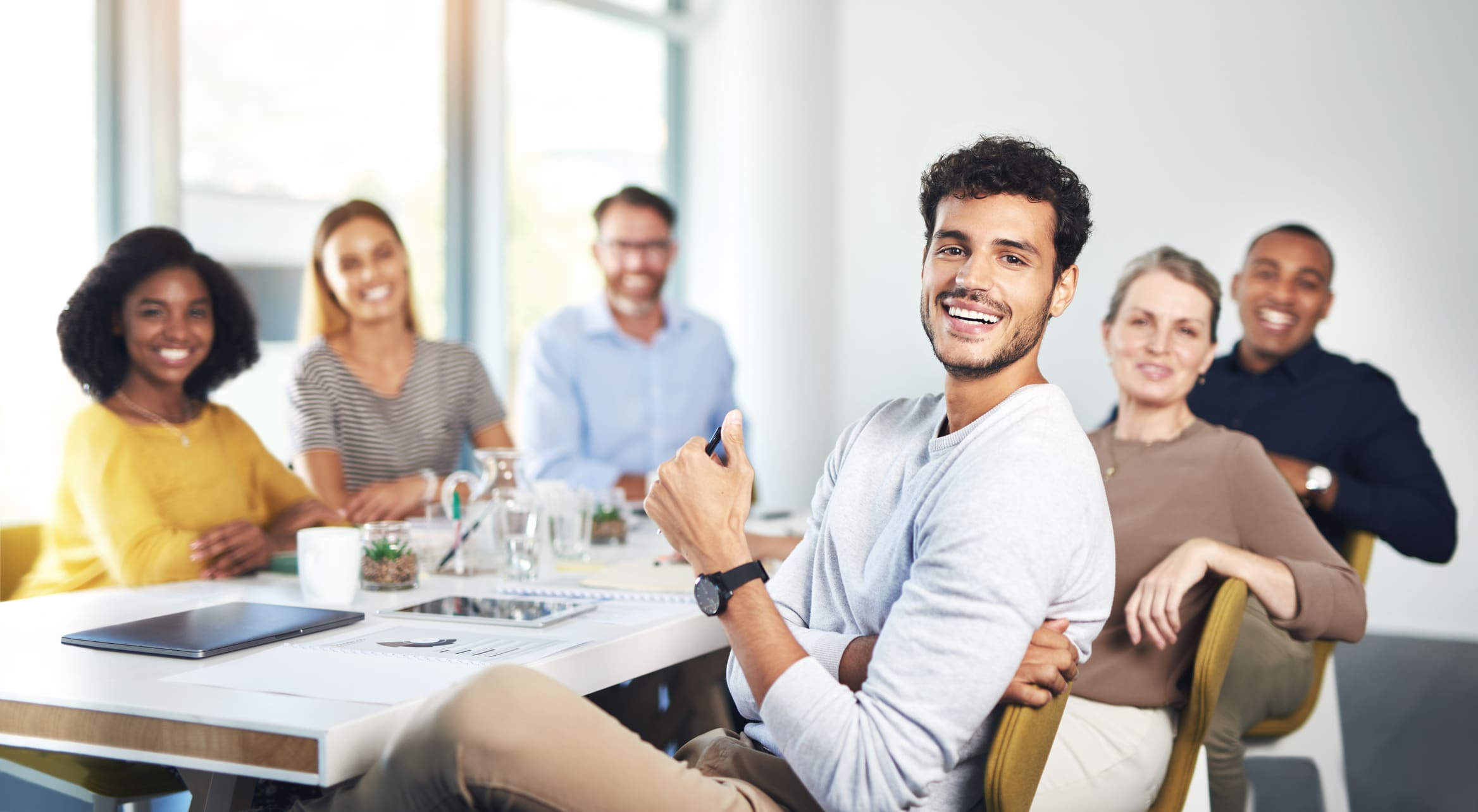An inclusive team gathered around a table with one man gesturing while discussing a project.