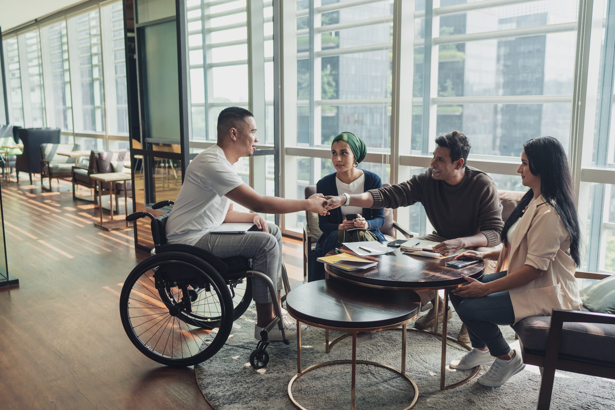 A diverse group of individuals gathered around a table, two of the people exchanging a handshake