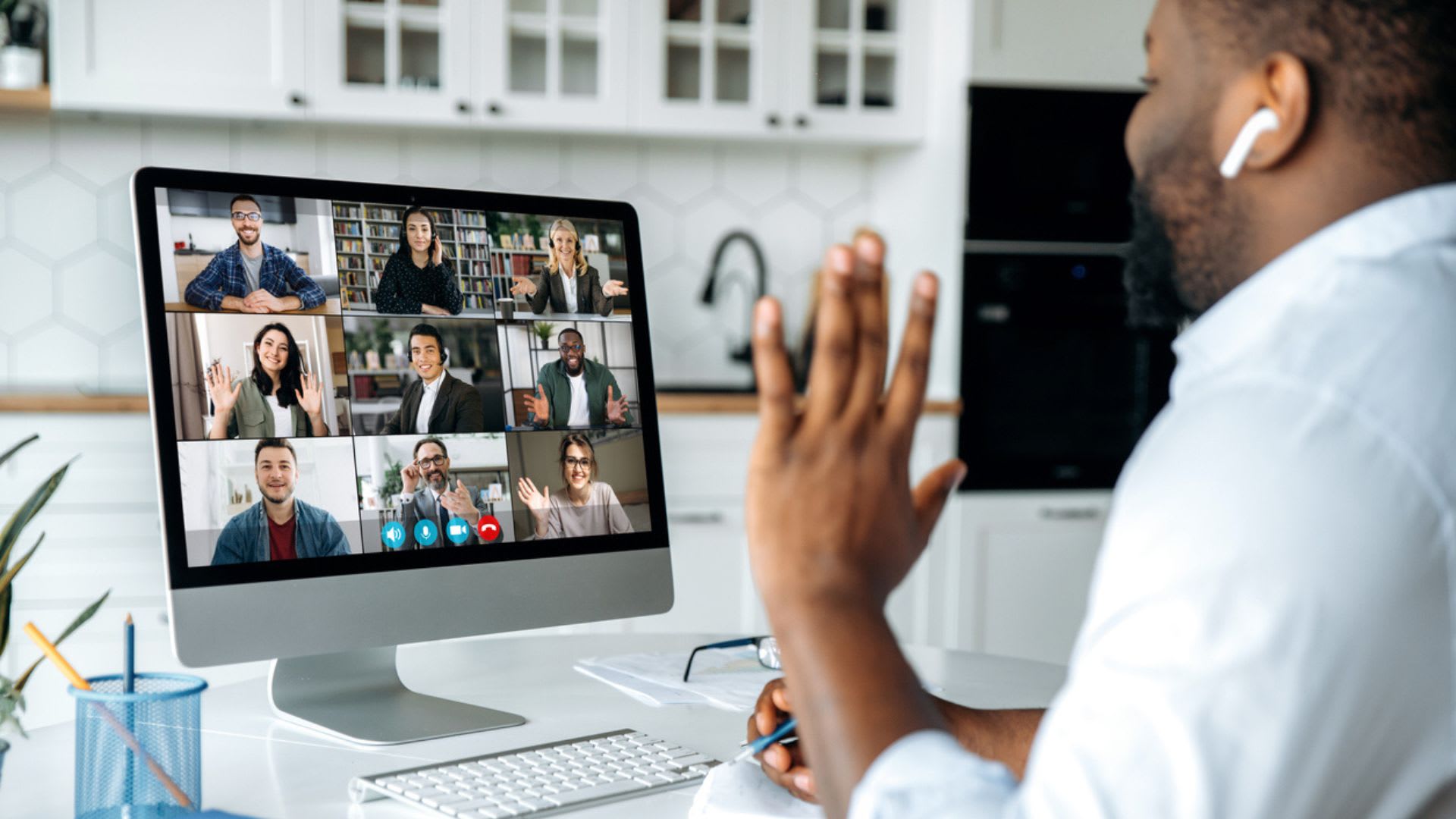 A man sitting at a desk with a computer screen displaying a group of people in a meeting.