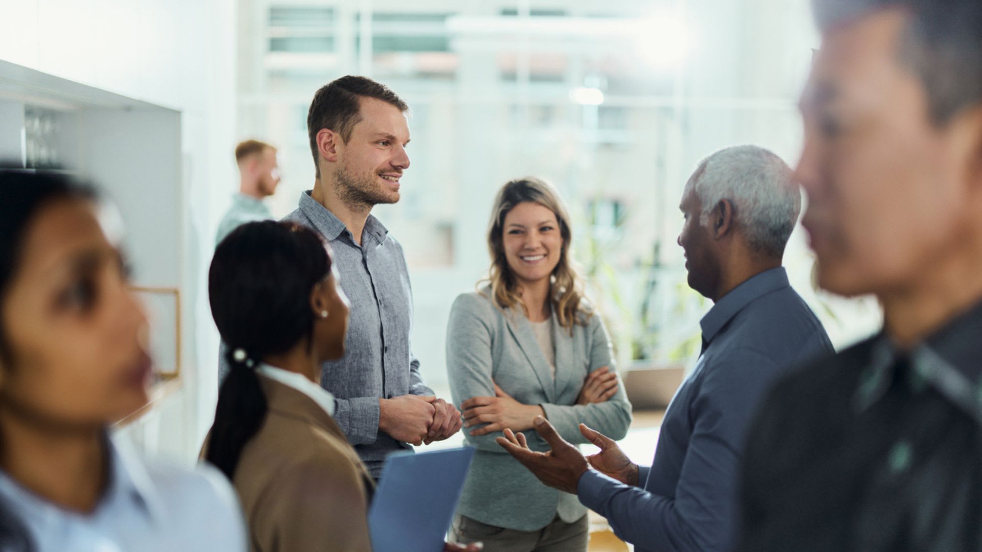 A diverse group of professionals standing together in a modern office, engaged in conversation and collaboration.