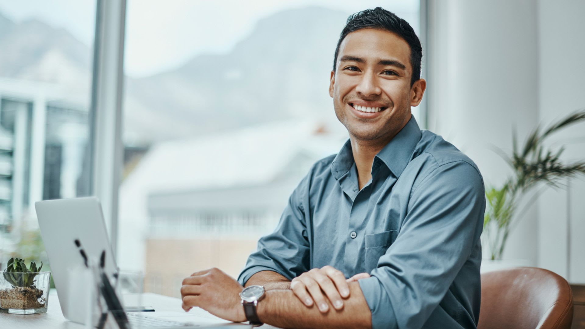 A man smiling while sitting at a desk with a laptop.